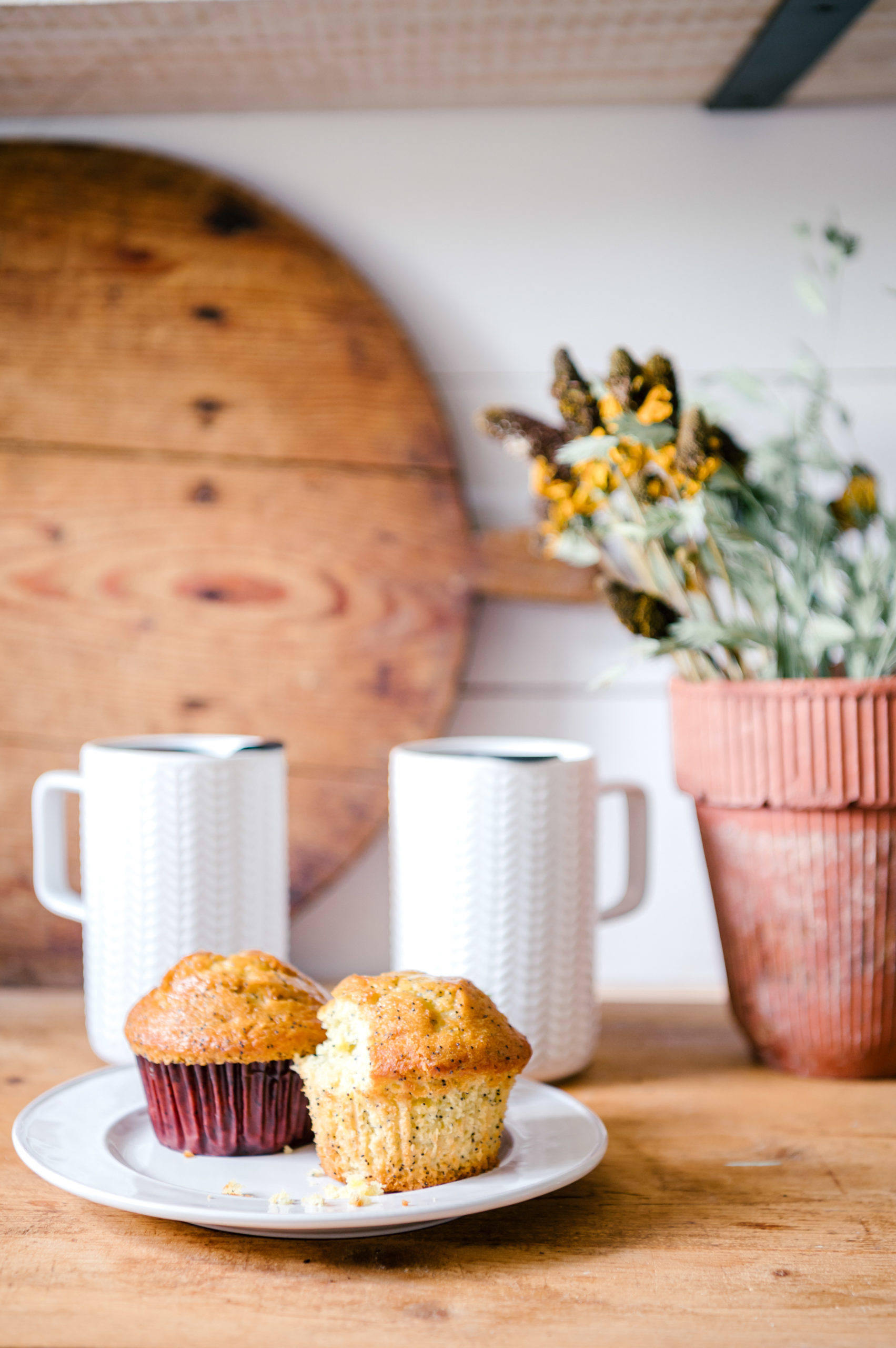 Muffins on white plate and two white mugs sitting on a wooden table