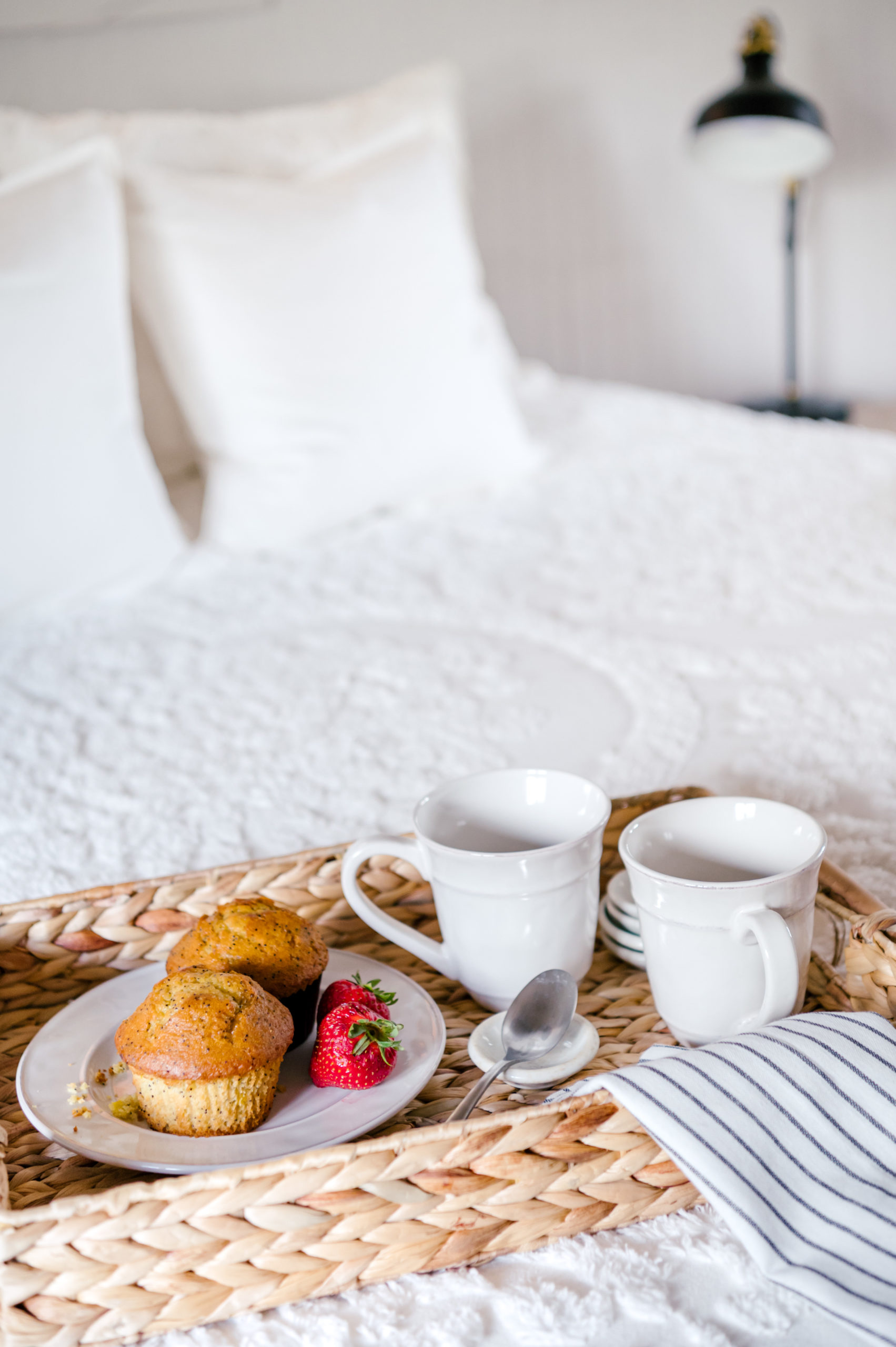 Breakfast tray with muffins, coffee mugs and striped napkin on white bed