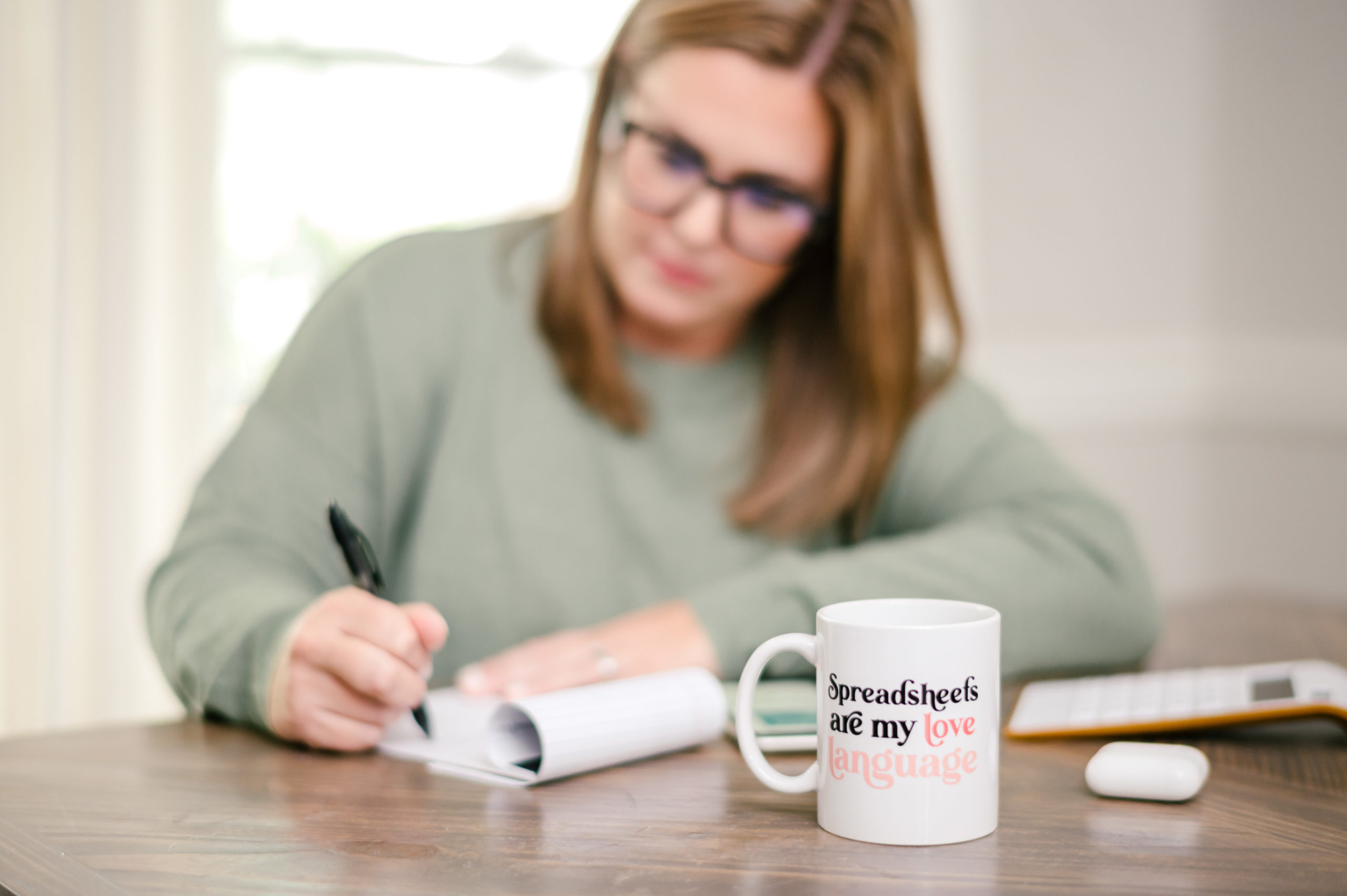 CPA business woman writing on notepad sitting next to a coffee mug that reads spreadsheets are my love language