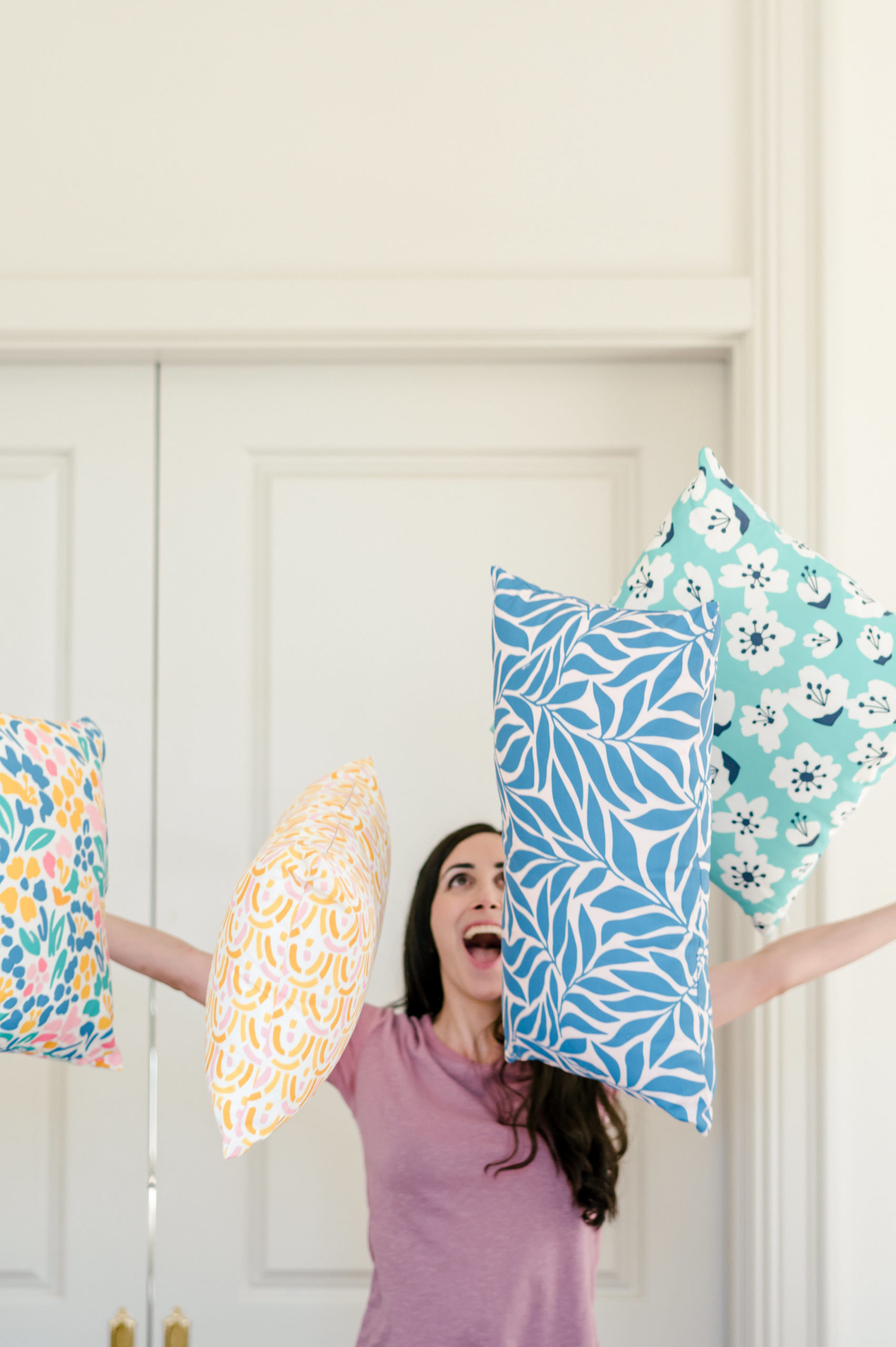 Woman designer throwing colorful pillows in the air that she designed herself smiling for her branding session