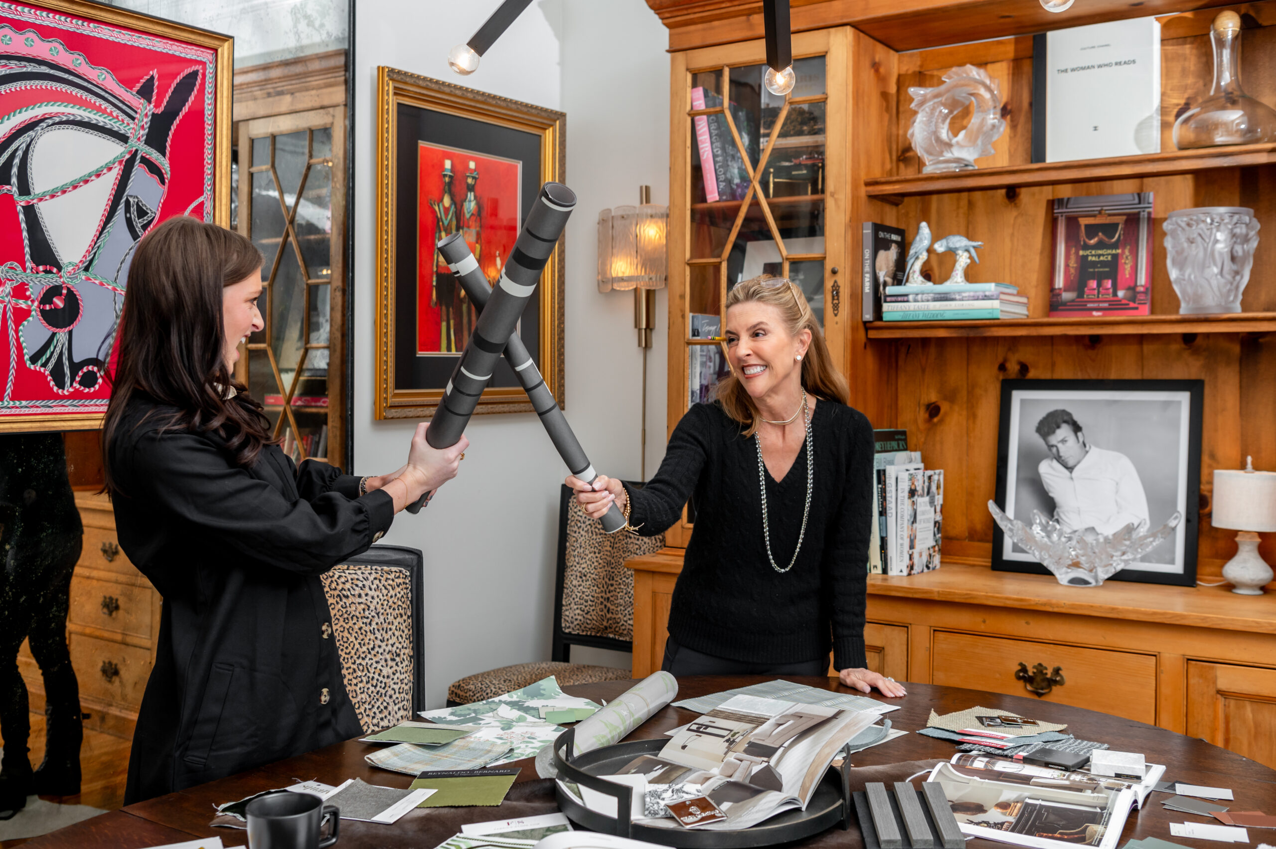 Two women interior designers fake fighting with a tube of paper