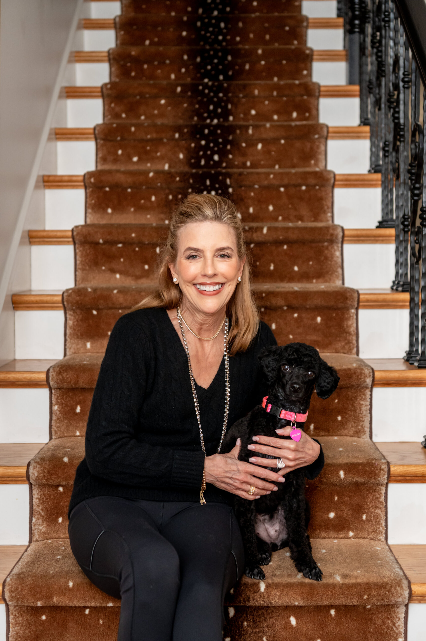 A women interior designer smiling holding her dog on a staircase for her interior design brand shoot