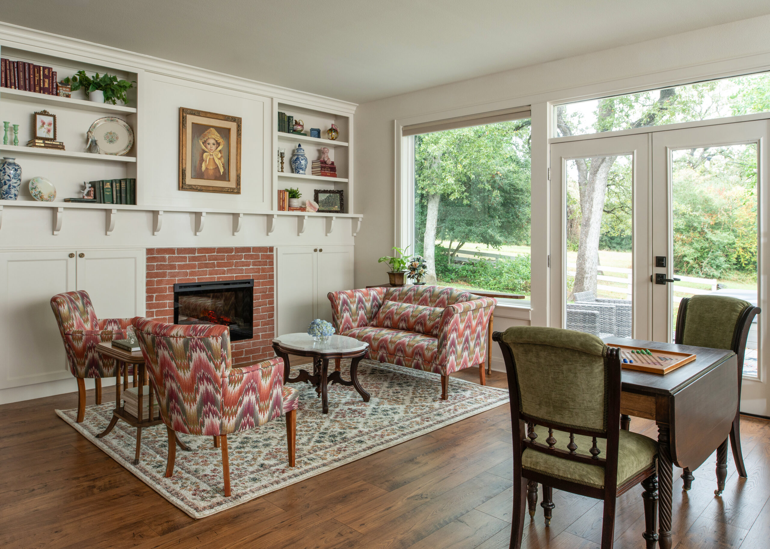 Cozy living room featuring a fireplace, comfortable seating with vibrant patterned chairs, and a small coffee table, surrounded by natural light. The space has a welcoming and warm atmosphere, showcasing timeless modern interior design.