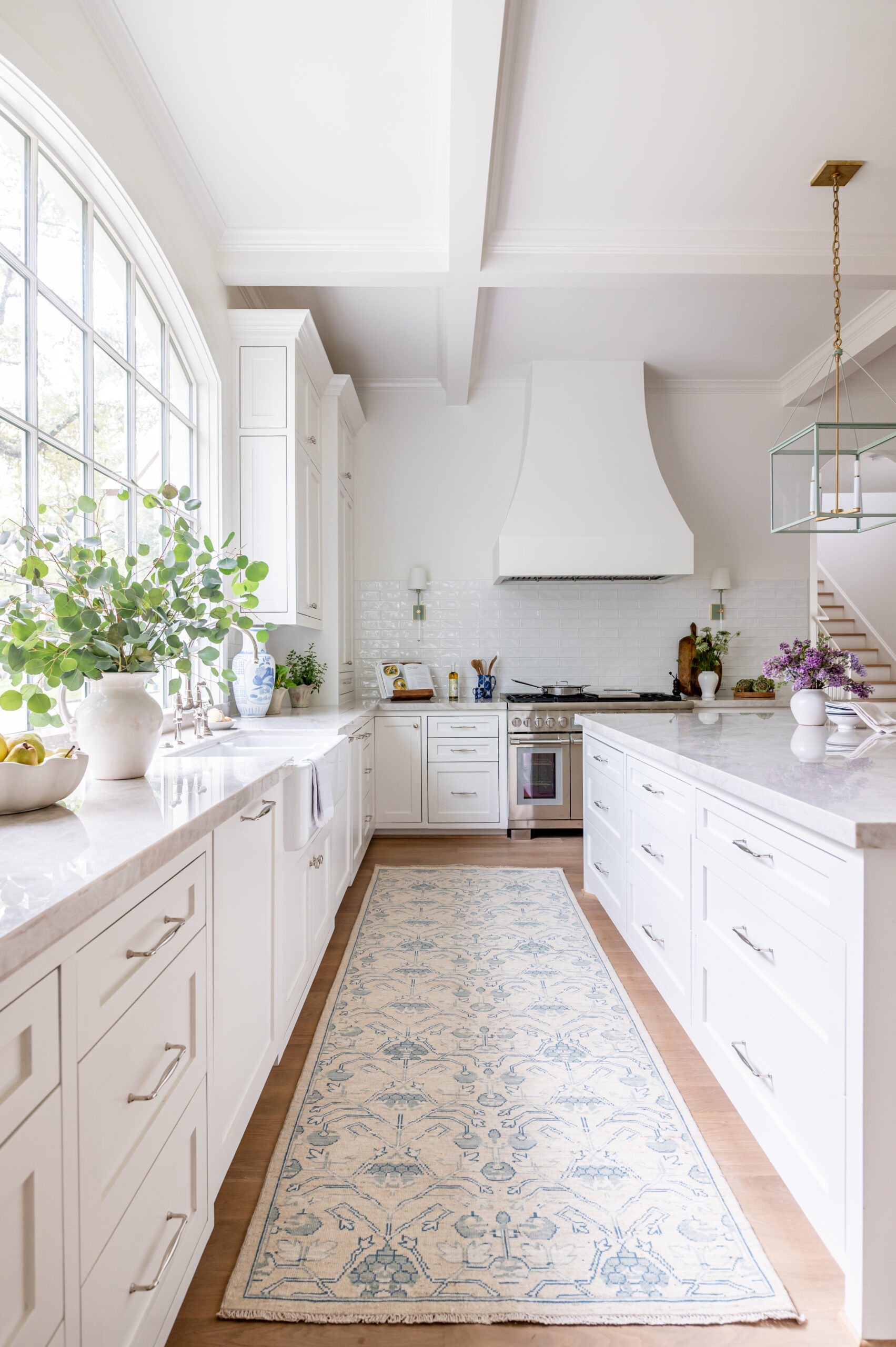 An elegant kitchen with white cabinetry, marble countertops, and stylish rattan bar stools, ideal for featuring in luxury interior design publications.