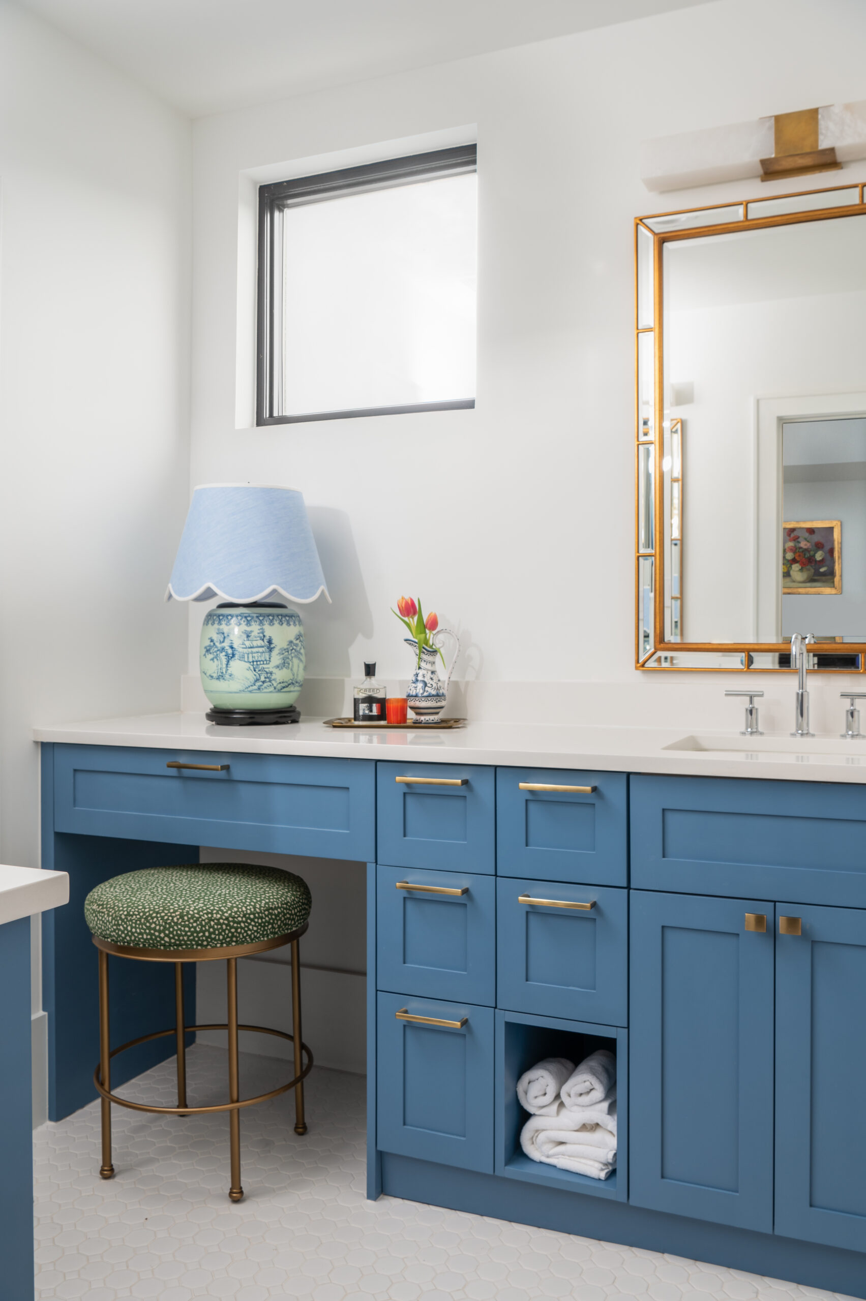 bright, blue bathroom with stylish cabinetry, a green patterned stool, and a light blue lamp, perfect for showcasing in interior design publications focusing on color accents and modern vanities