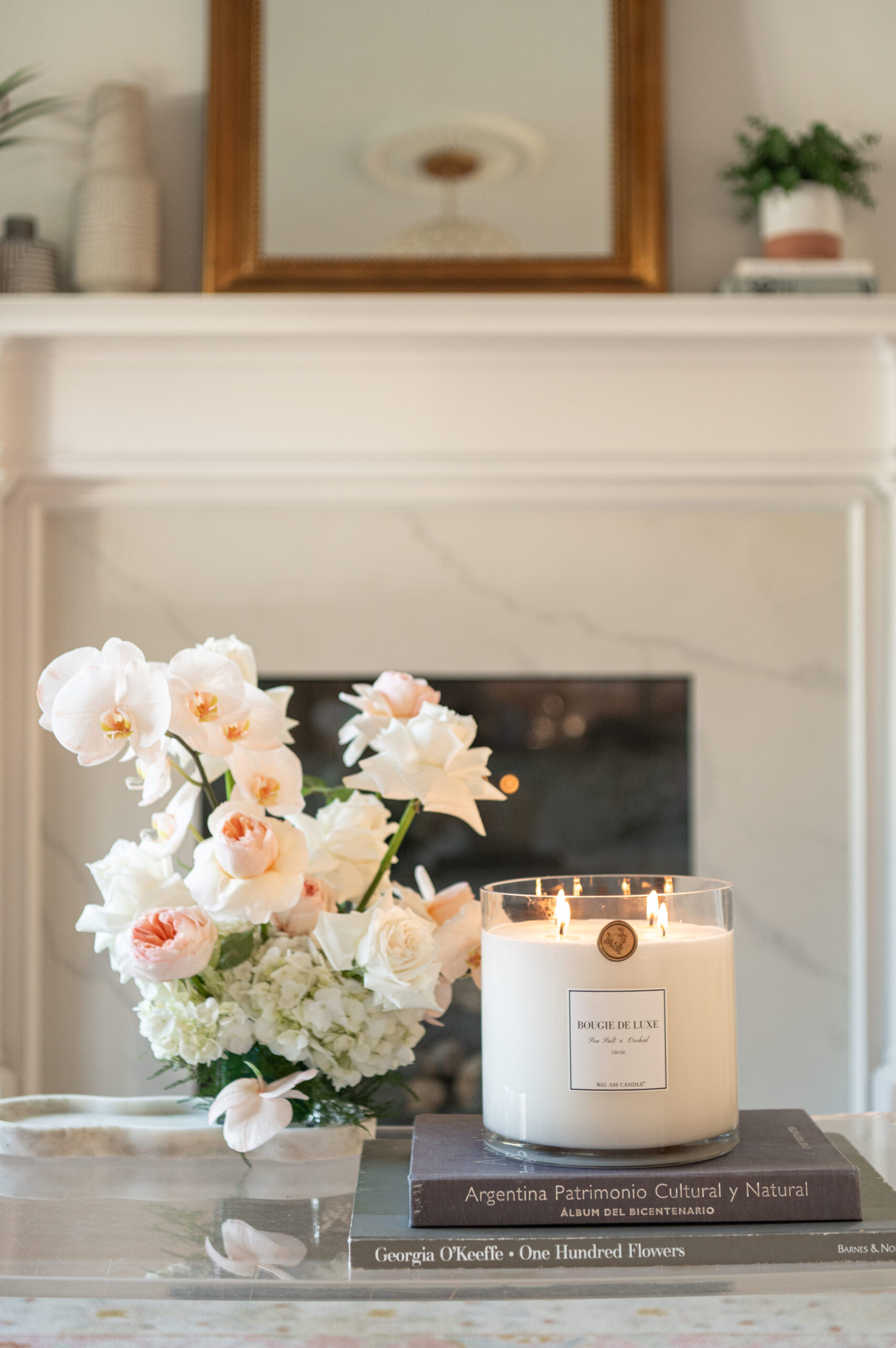 A stylish living room with a fireplace, decorated with white flowers, a lit candle, and seasonal decor, capturing a peaceful, elegant setting for seasonal photography that embodies comfort and home beauty.