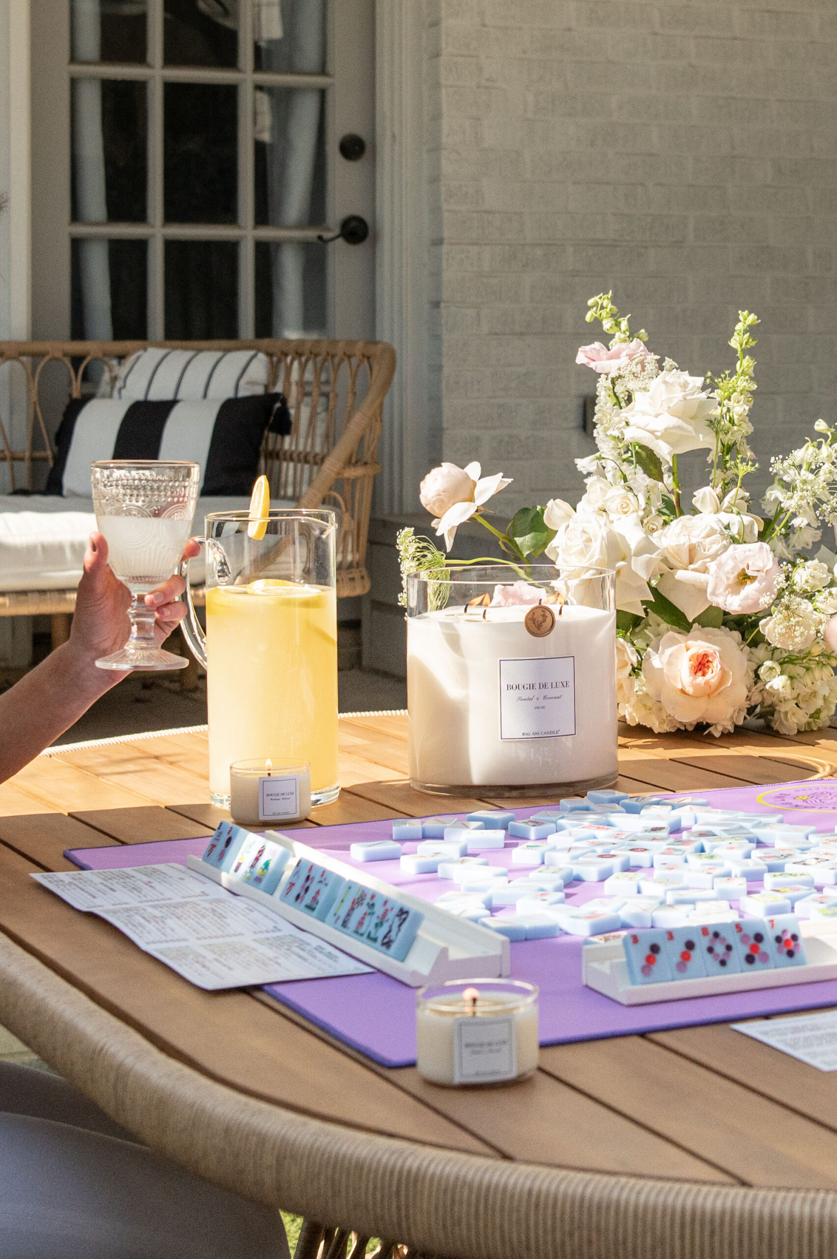 A group of friends enjoying a game of Mahjong outside with a beautiful floral arrangement and a candle burning, captured in a moment of seasonal photography for a spring branding shoot.
