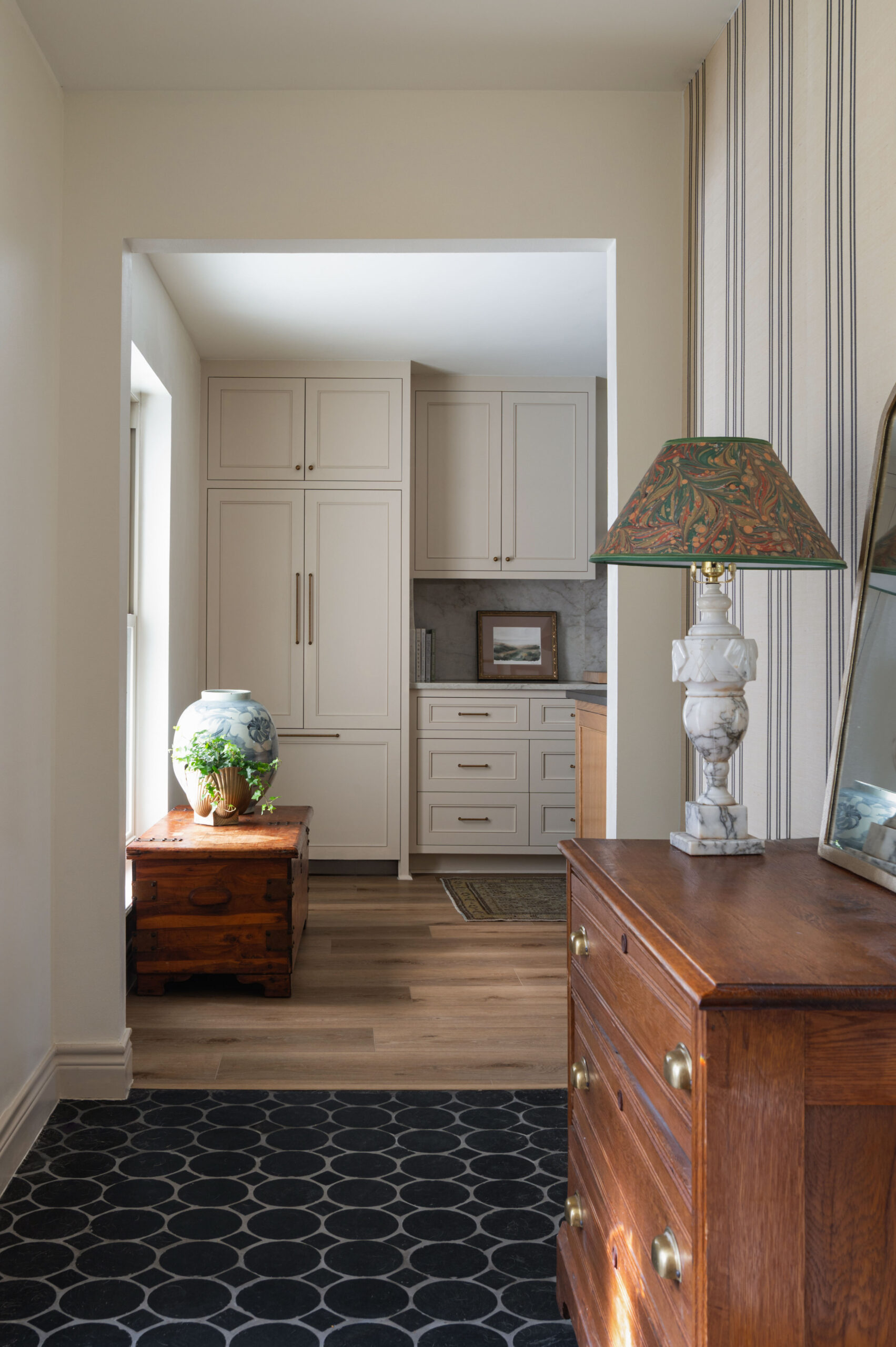 View through a transitional space into a kitchen with neutral cabinetry, vintage chest, and striped wallpaper—an ideal scene for understanding how to photograph interior spaces with depth and balance.