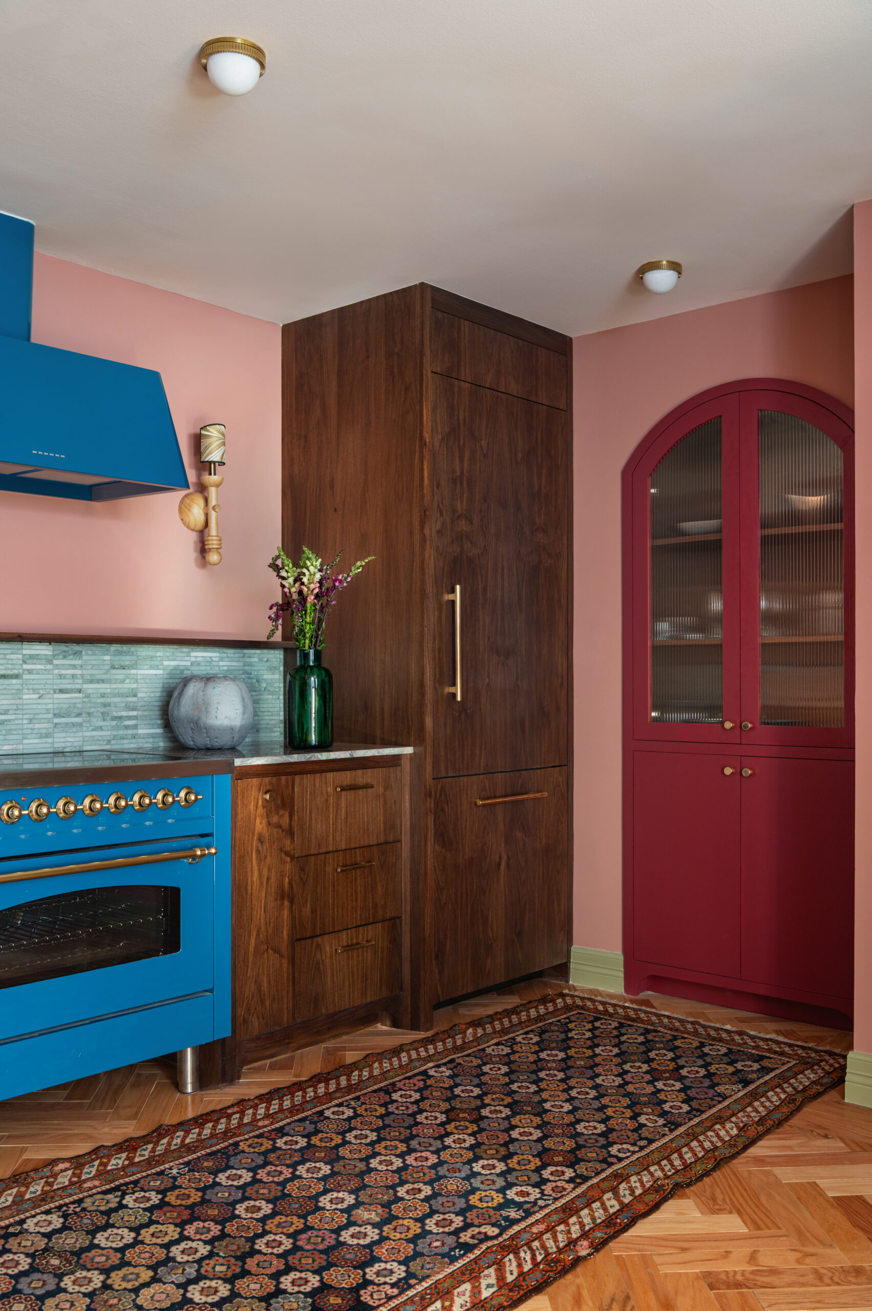 Rich walnut cabinetry paired with a bold blue range and vent hood in a pink-walled kitchen—an example of how to photograph interior spaces using color contrast to draw focus.