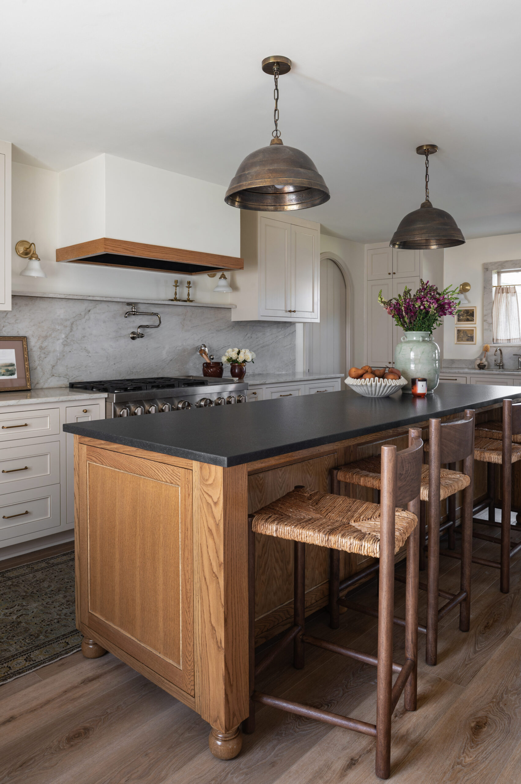 Center island kitchen with matte black counters, oak cabinetry, and woven stools under moody industrial pendants—great reference for how to photograph interior spaces with varied textures and lighting.