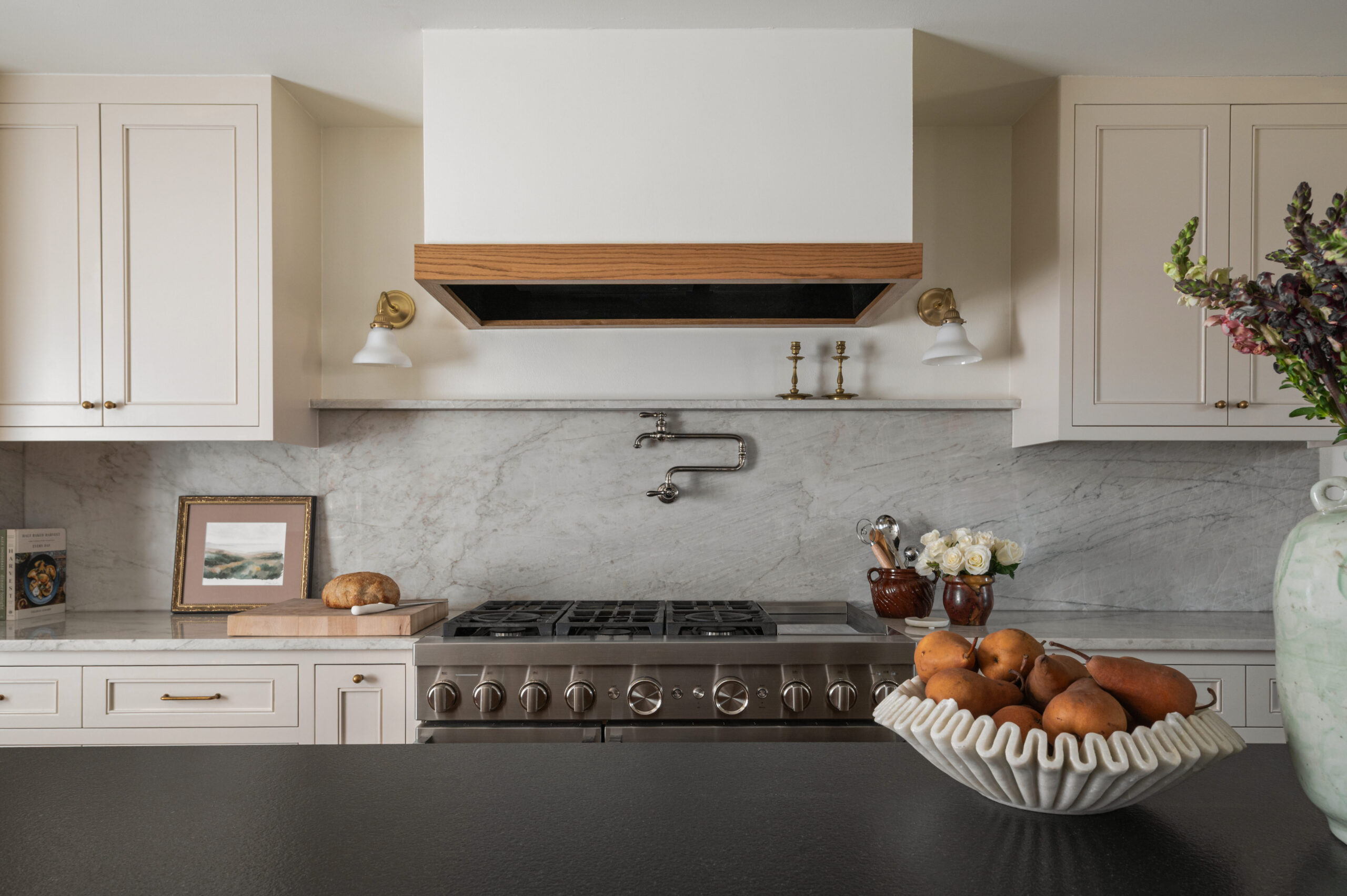A centered kitchen vignette with a stainless steel range, marble backsplash, and decorative accents like candlesticks, fresh bread, and floral arrangements—highlighting balance and storytelling in kitchen photography.