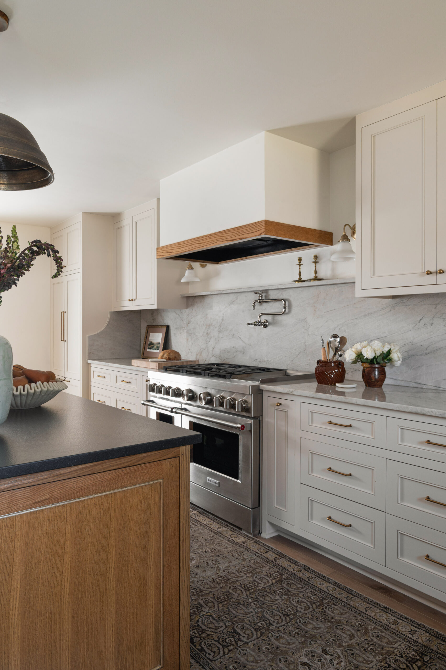 A detail view of a classic kitchen with a marble backsplash, creamy cabinetry, and a stainless steel range, styled with vintage decor and warm wood accents.