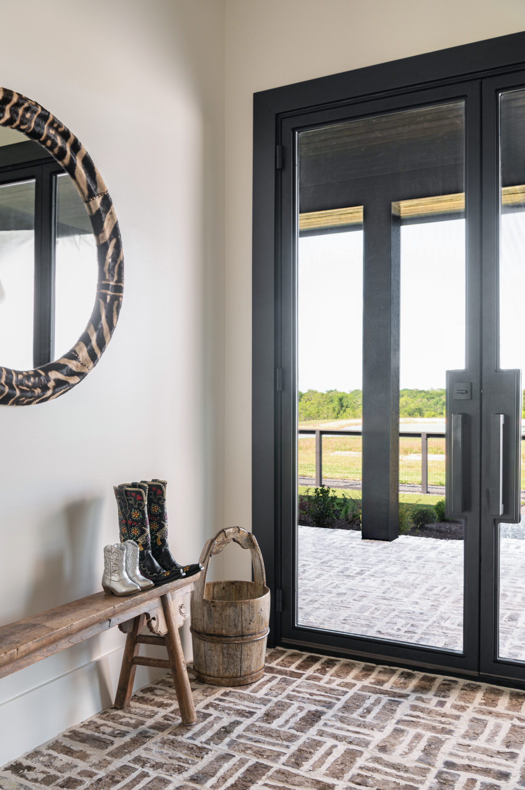 A welcoming mudroom entry with a vintage wooden bench, cowboy boots, a rustic bucket, and a round zebra-patterned mirror, tying country flair into a contemporary space.