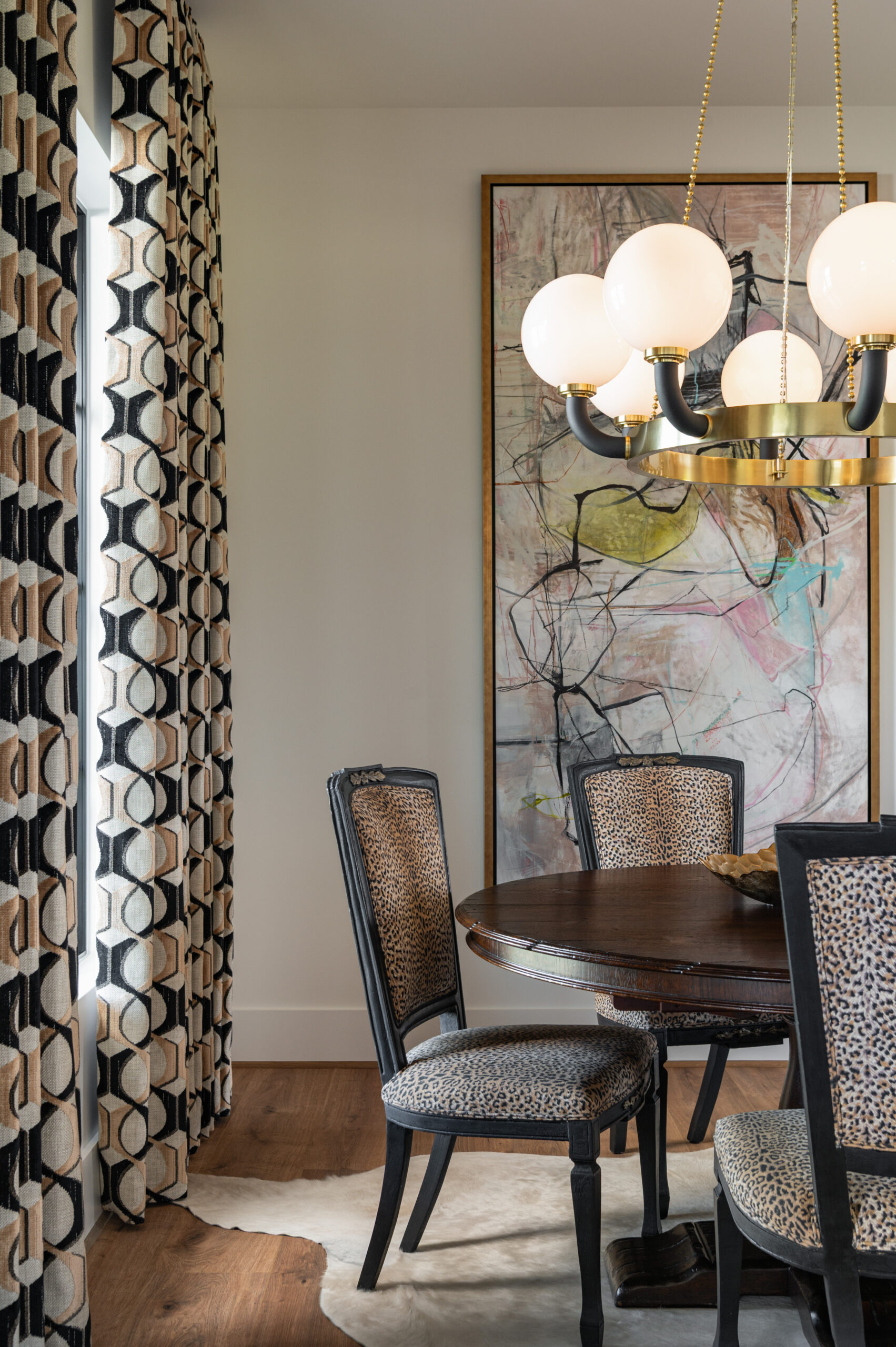Visual storytelling photography of an eclectic dining area showcasing leopard-print chairs, a round wooden table, dramatic drapes, and abstract wall art that adds personality and movement.