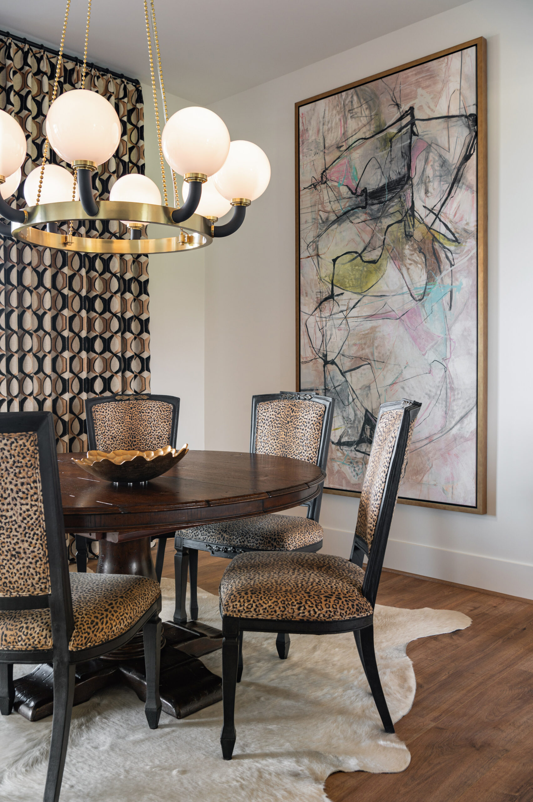 Visual storytelling photography of a bold dining space featuring leopard print chairs, a round wood table, abstract artwork, and retro-style patterned drapes.