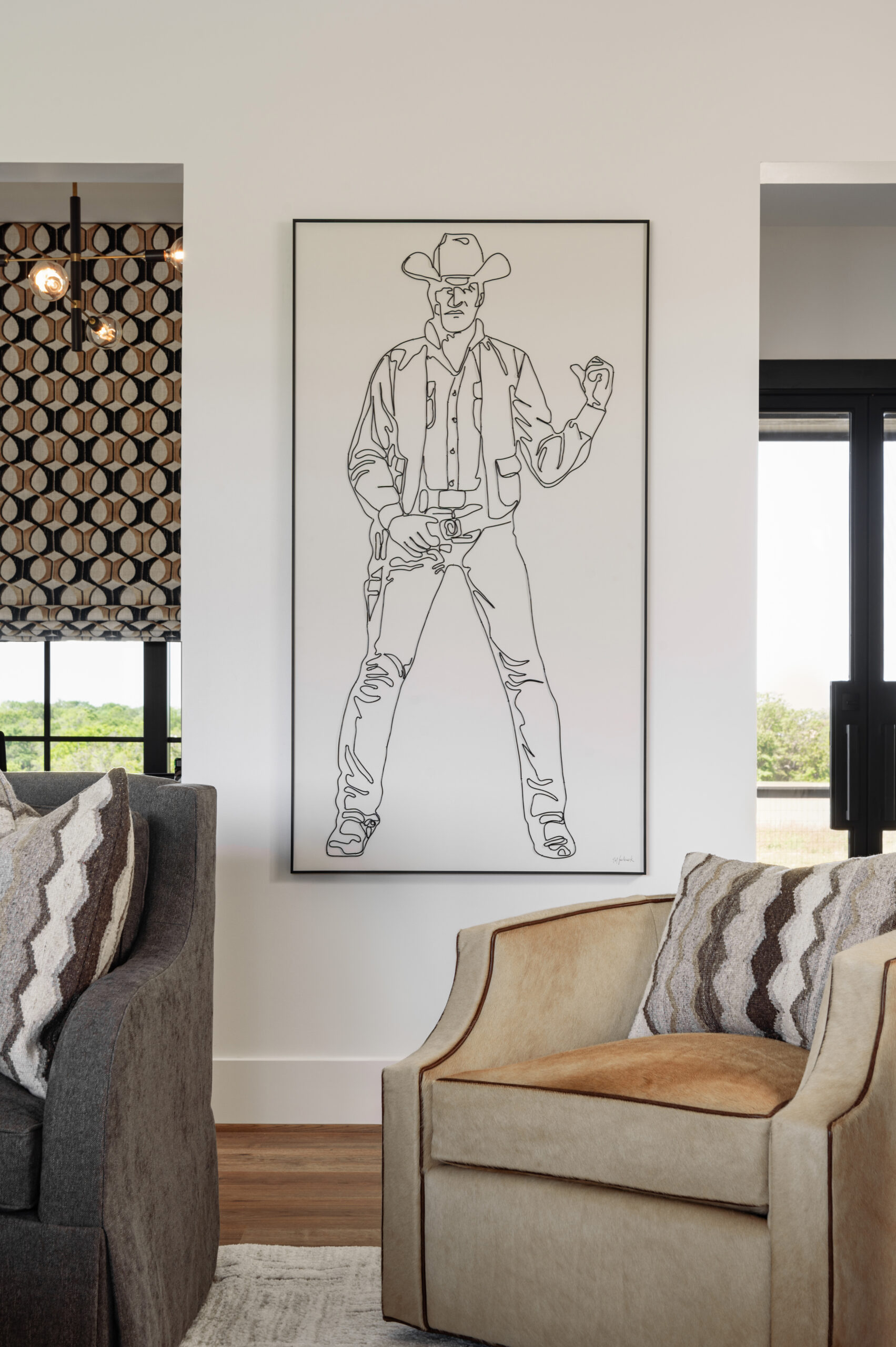 Visual storytelling photography of a minimalist line art drawing of a cowboy, framed in black and placed beside a cozy living room setup, blending western influence with modern aesthetics.