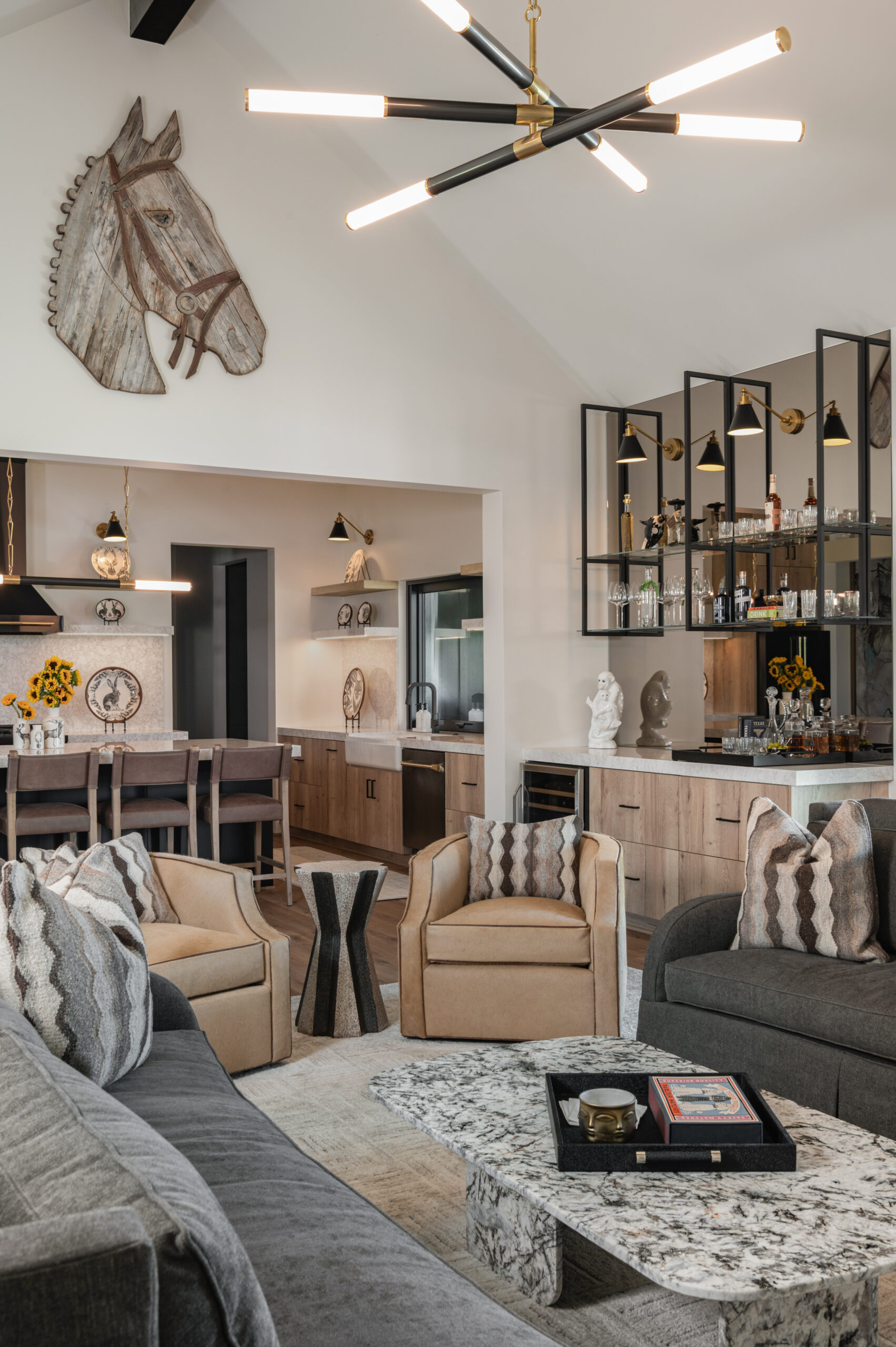 A cozy yet refined living room with modern lighting, earthy-toned seating, and a bold horse head sculpture above a wide entryway, blending rustic charm and luxury.