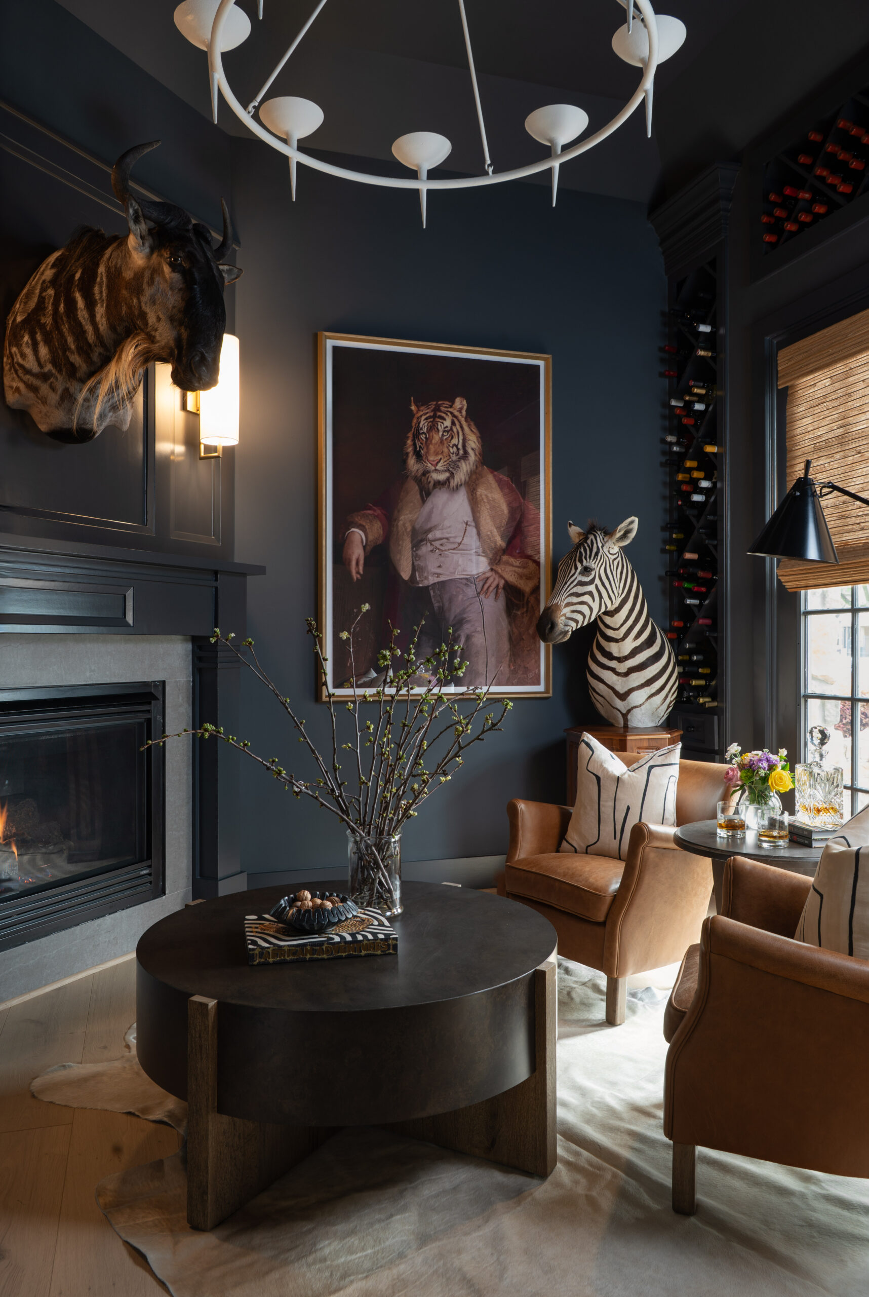 A dramatic sitting area with navy blue walls, mounted taxidermy, and a striking tiger portrait; warm leather chairs and a zebra bust create a bold focal point in this portfolio for interior design.