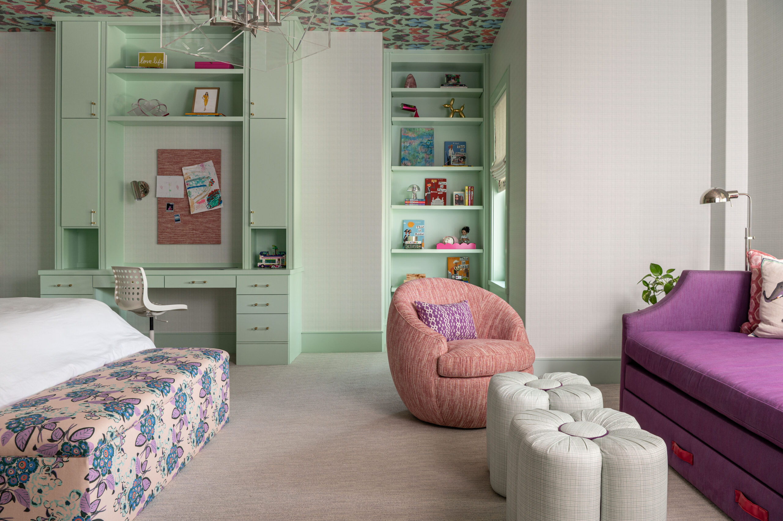 A cozy corner of a tween bedroom featuring a blush swivel chair, mint green built-ins, and playful ceiling wallpaper.