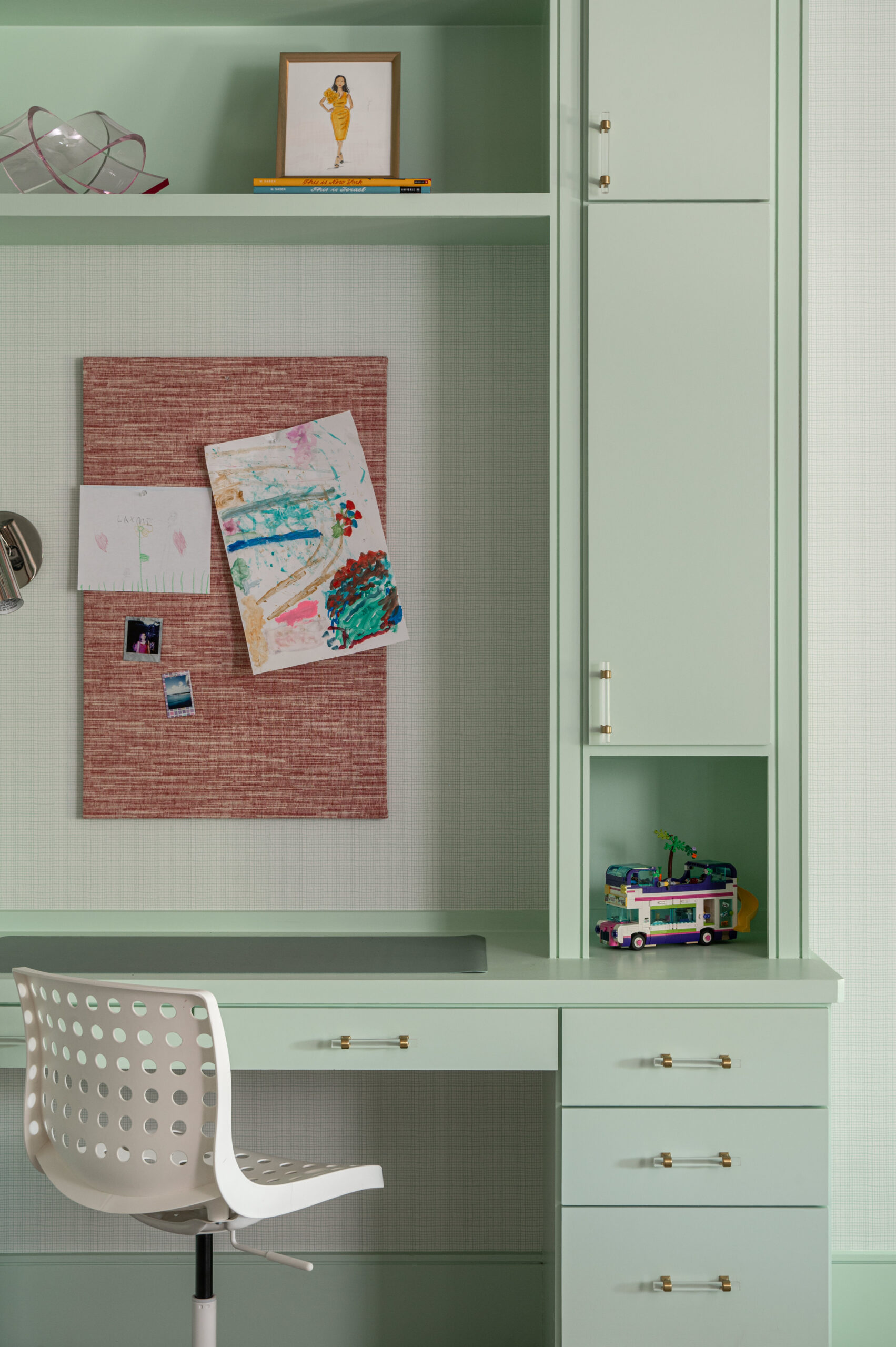 A close-up of a mint green desk with a pinboard displaying children's artwork and a small toy camper van.