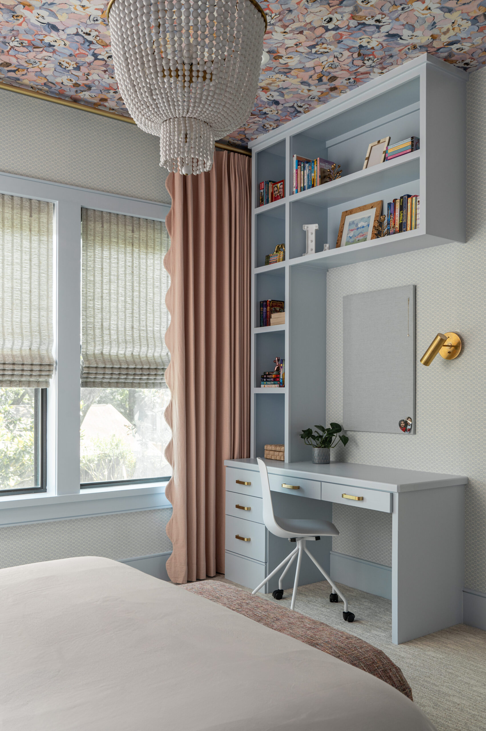 A pastel blue desk built into the corner of a tween bedroom with shelves full of books and a modern white desk chair.