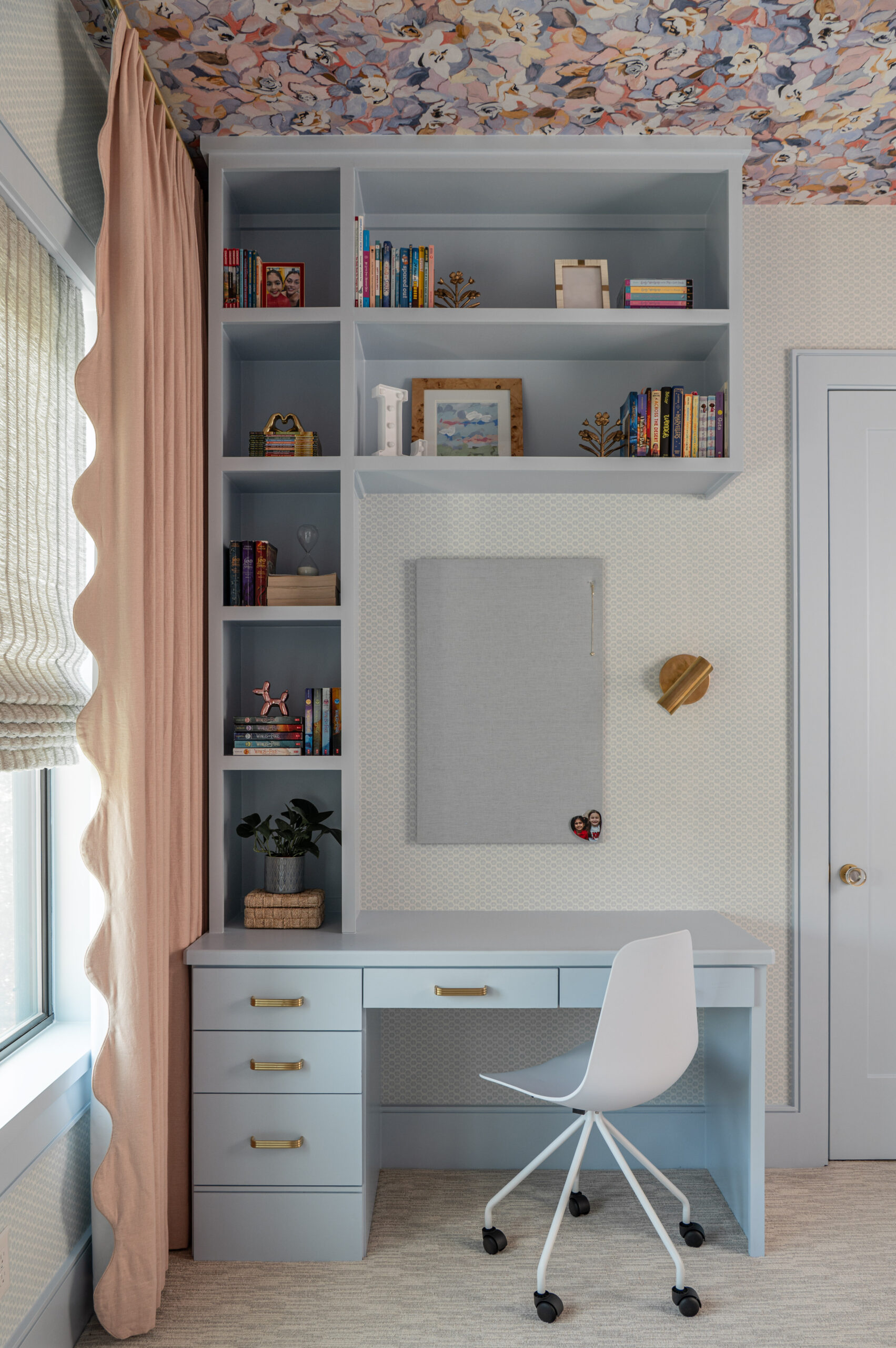 A pastel blue desk built into the corner of a tween bedroom with shelves full of books and a modern white desk chair.