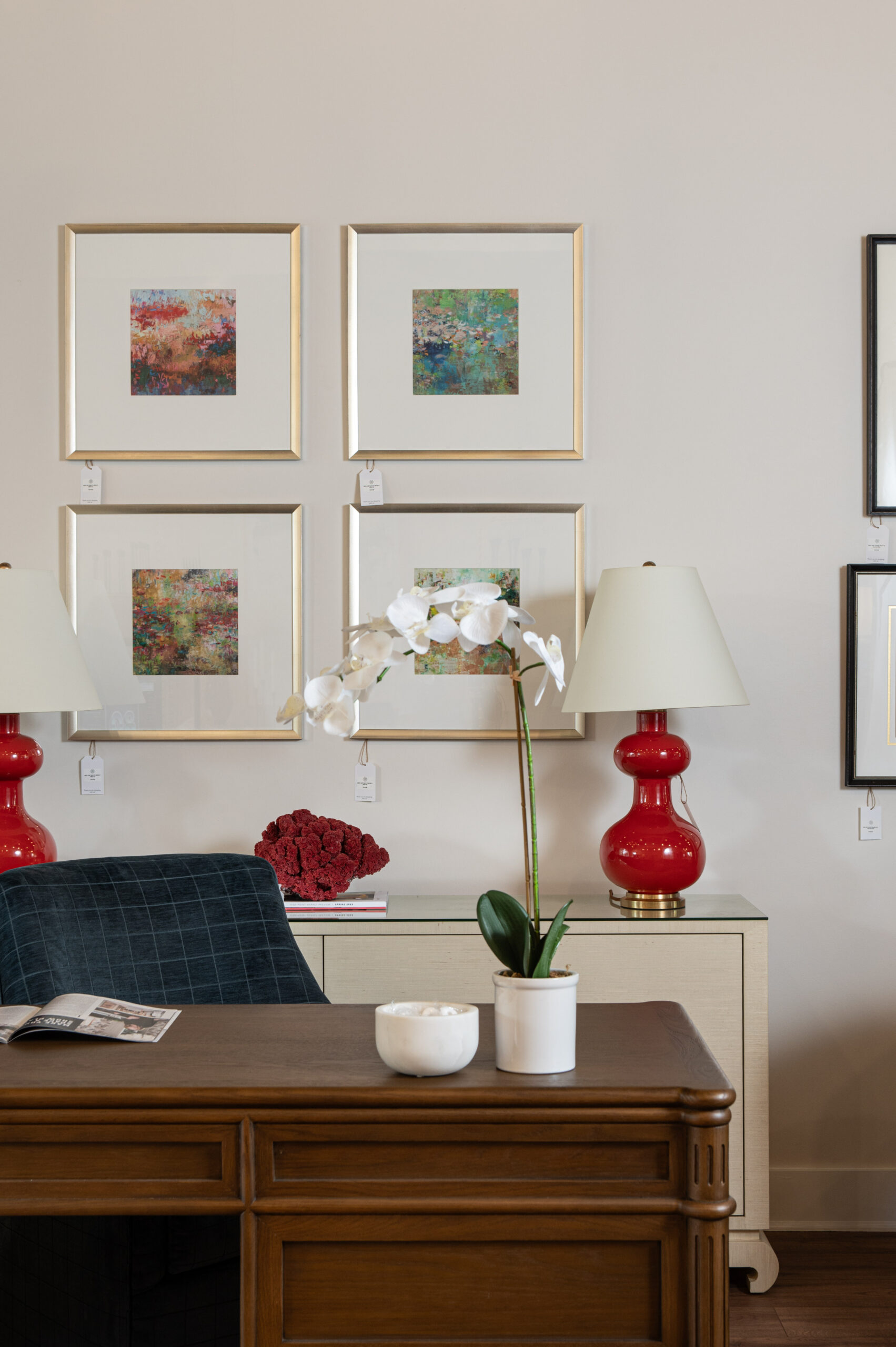 Orchid centerpiece on a wood desk with bold red table lamps and framed abstract prints in a cozy office vignette.