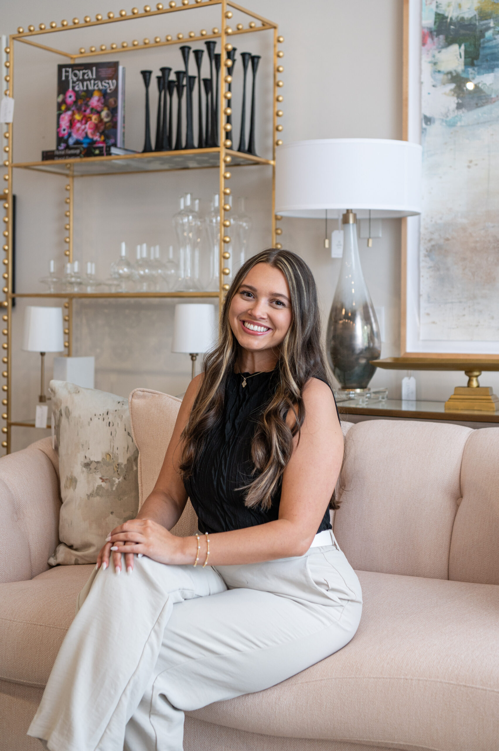 Interior designer sitting confidently on a neutral sofa with styled shelving in the background, captured as part of a brand photography session.

