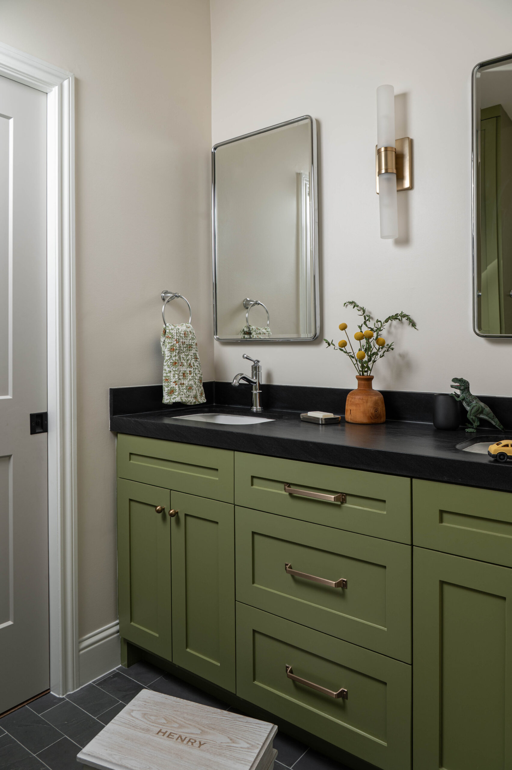 Bathroom vignette with olive cabinetry, black countertops, and delicate yellow florals styled in a wooden vase—example of vignette photography for interior design.