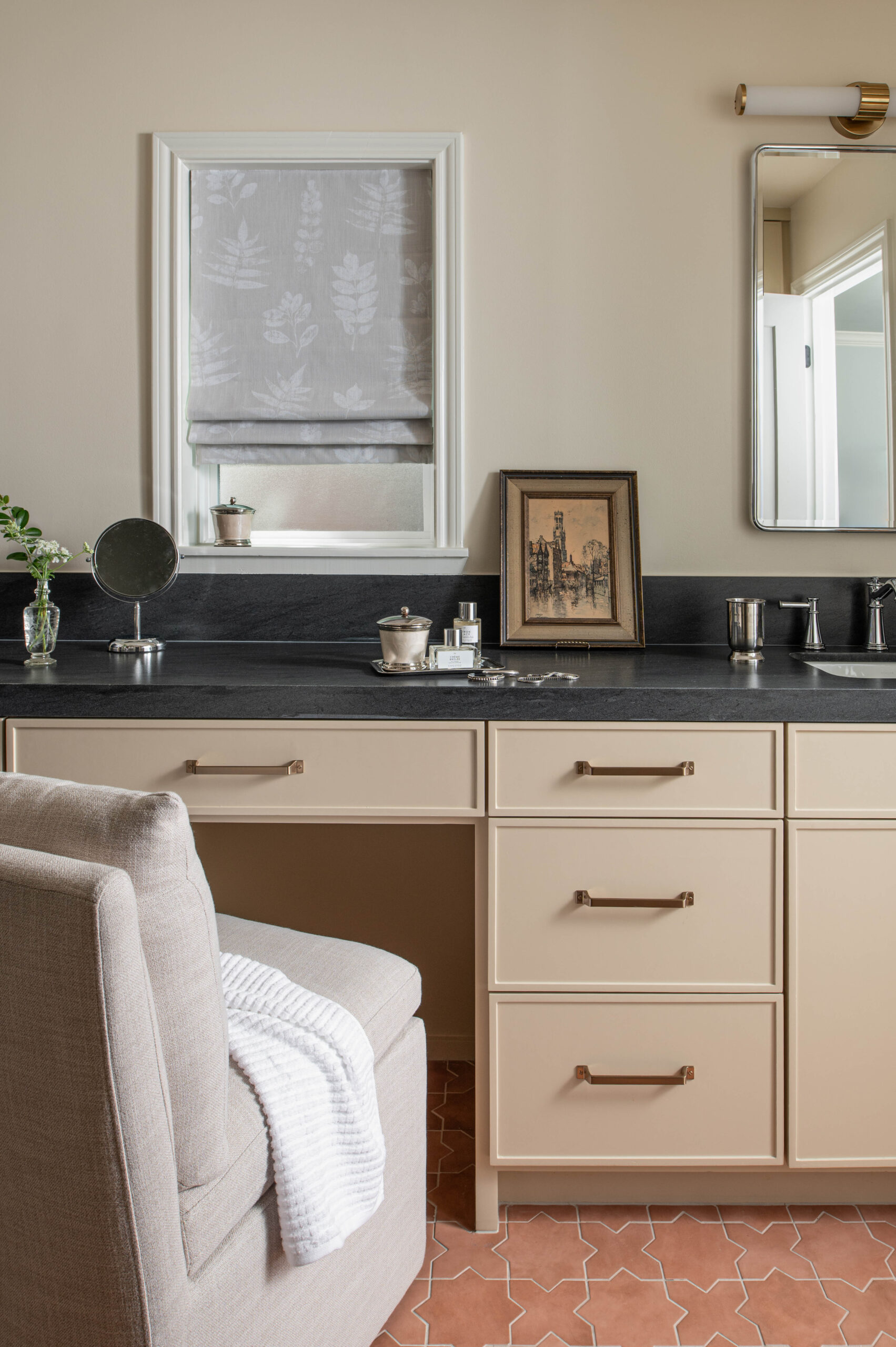 Elegant vanity vignette with a neutral palette, black stone counters, and framed artwork leaning casually near a makeup mirror.