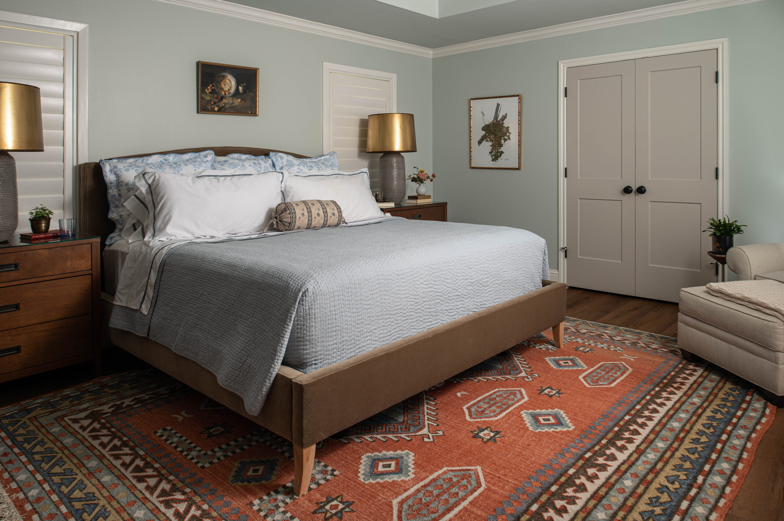 Warm-toned bedroom with a patterned red rug, upholstered bed, and traditional decor in a cozy modern cottage.