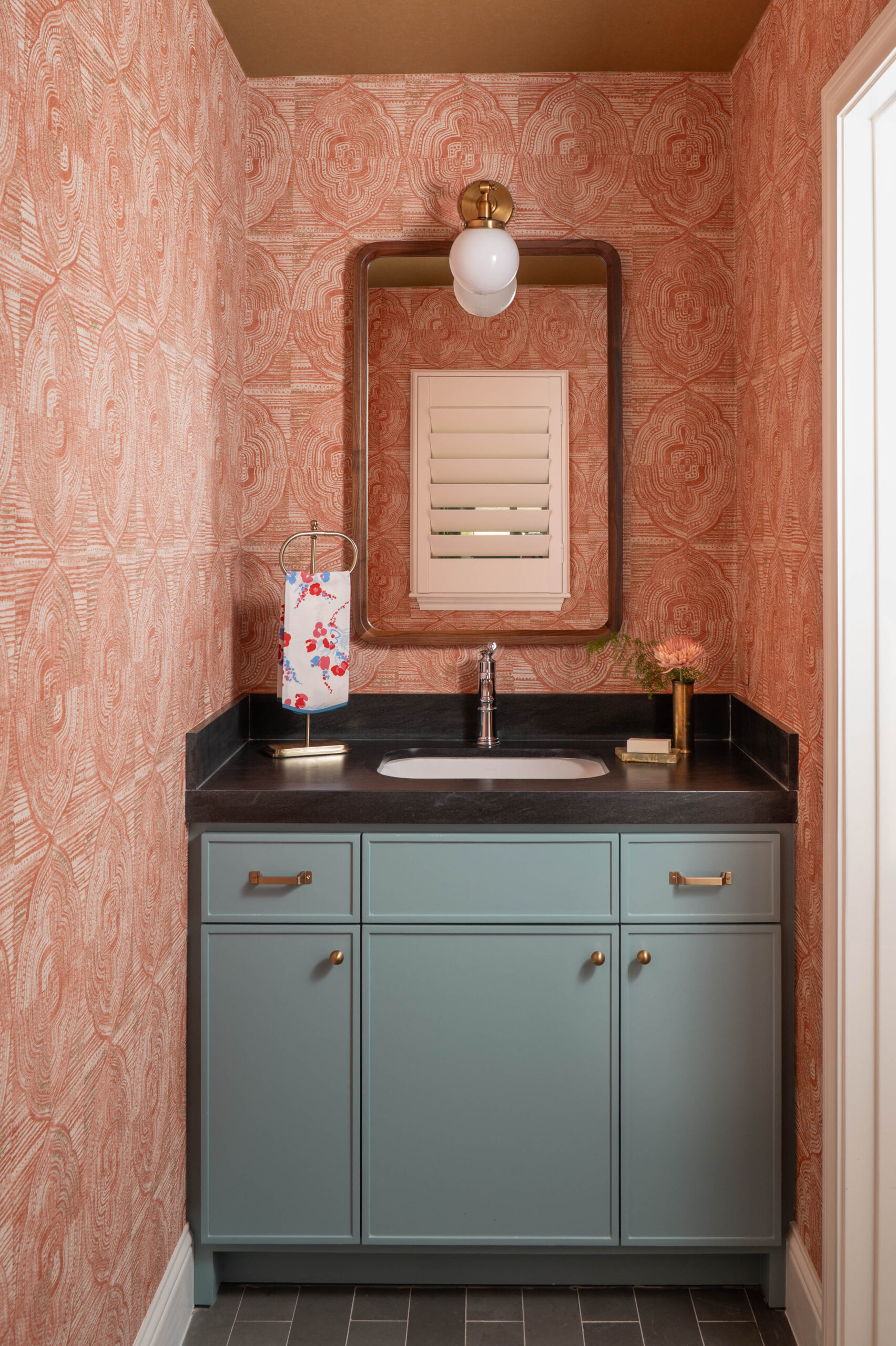 Bold powder room design featuring a teal vanity, graphic coral wallpaper, and curated brass accents—captured with a vignette photography approach.