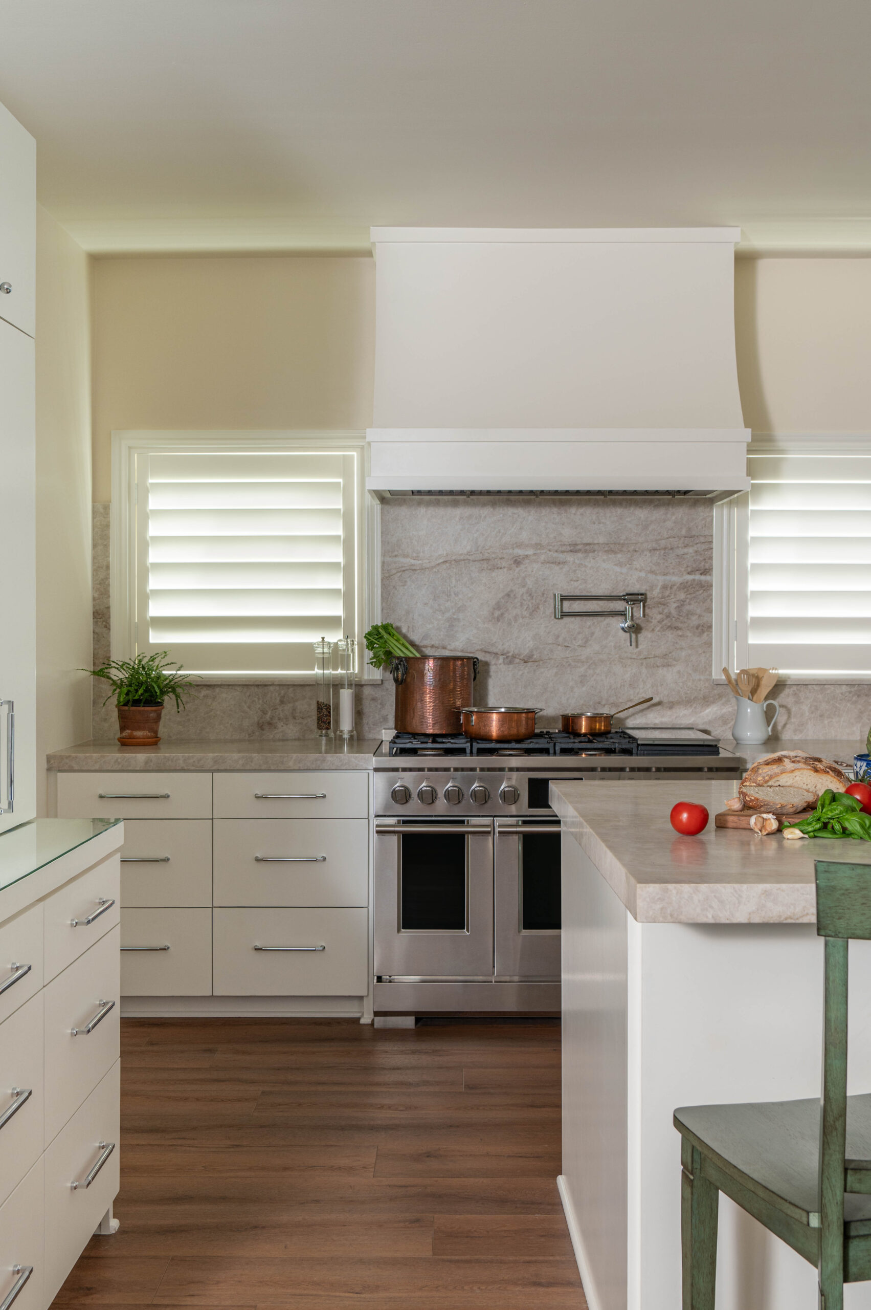 Close-up of a kitchen range with copper cookware, natural stone backsplash, and fresh produce on the counter.