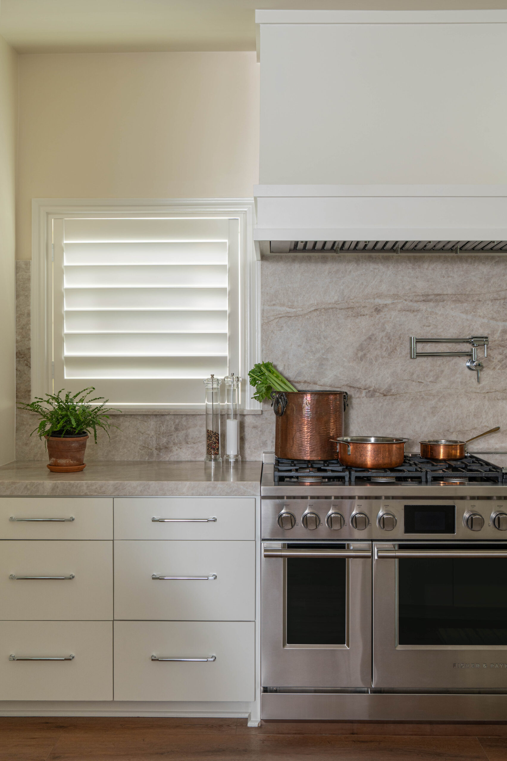 Close-up of a kitchen range with copper cookware, natural stone backsplash, and fresh produce on the counter.