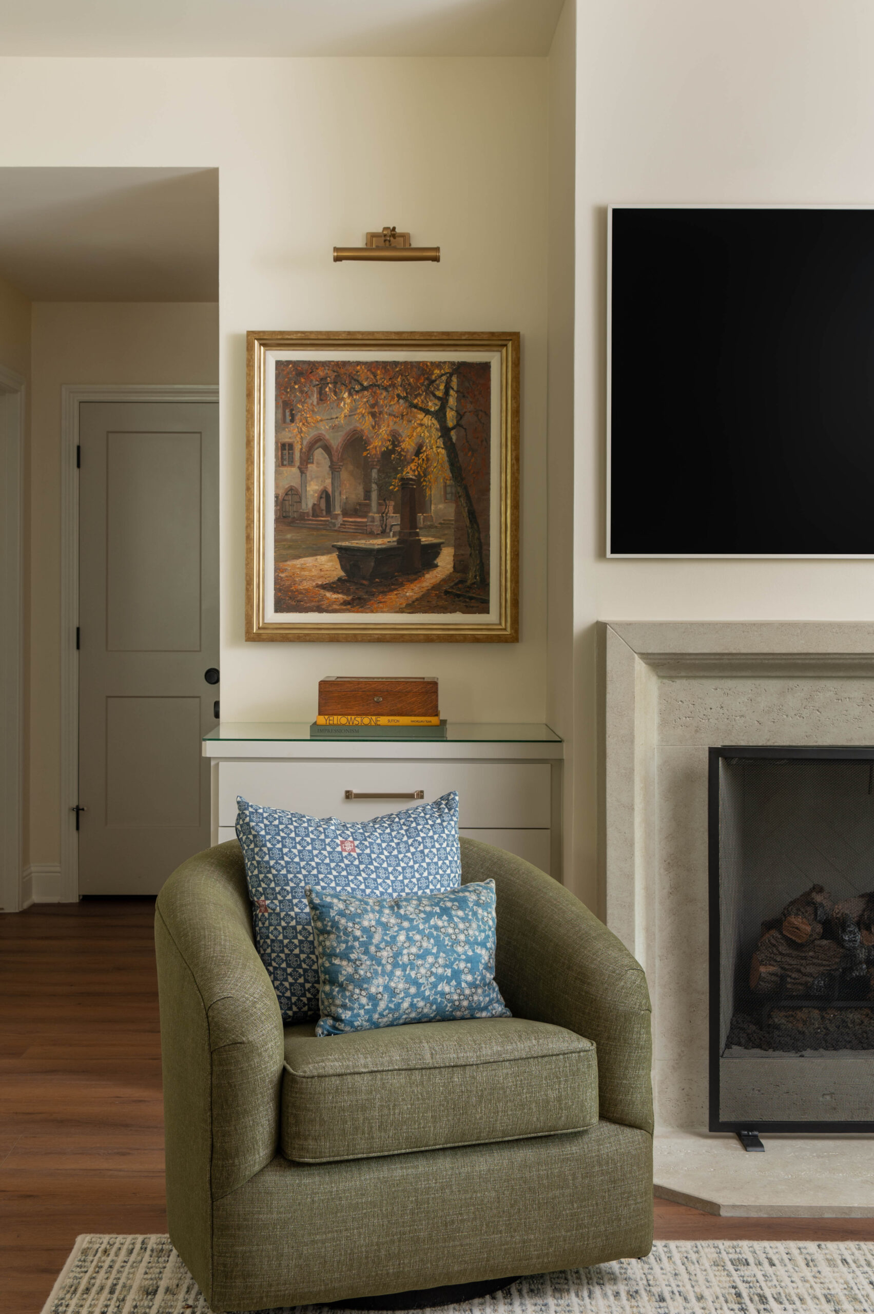 Vignette photography of a cozy reading corner with an olive green chair, blue floral pillows, and classic autumnal artwork.