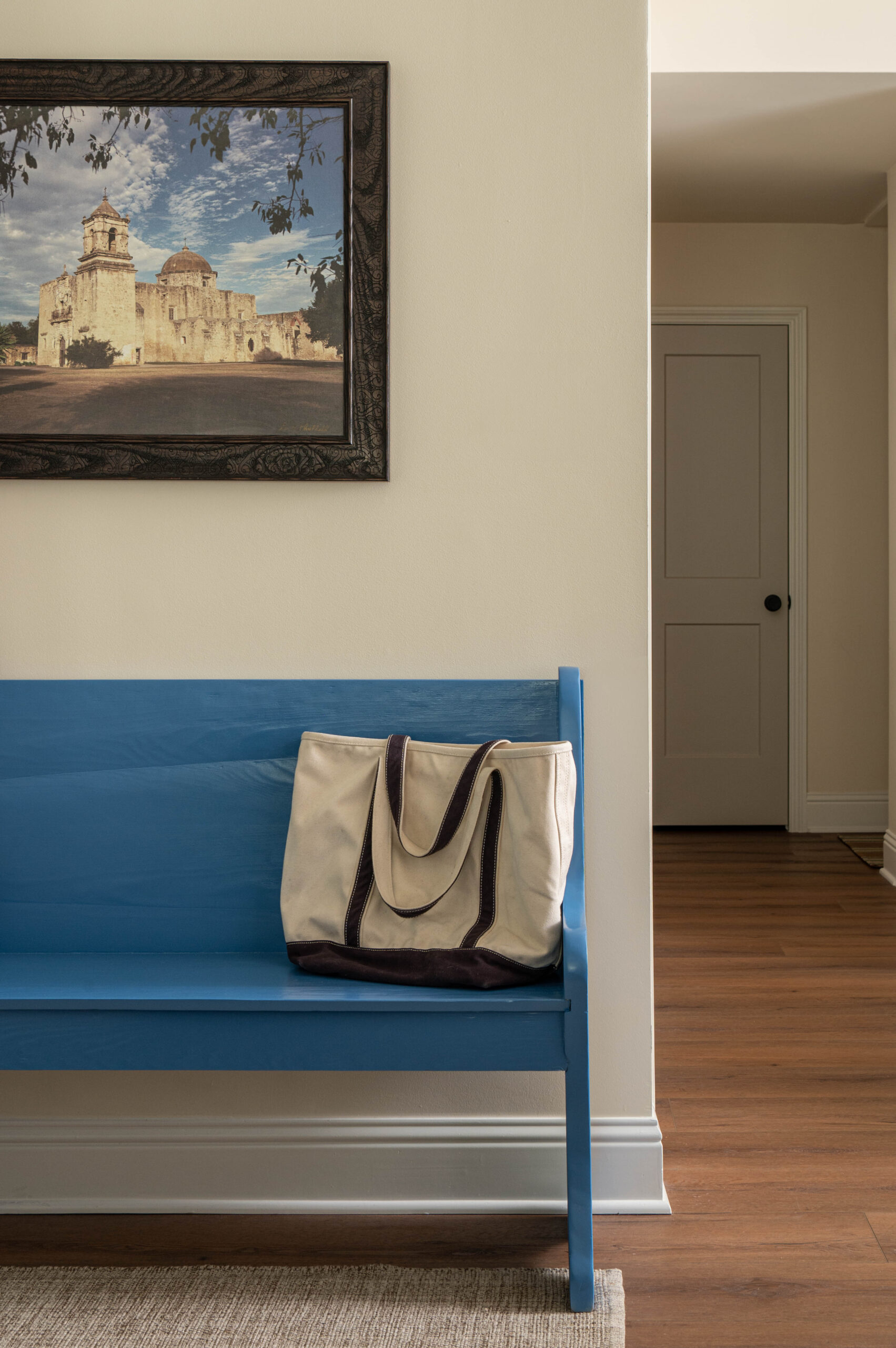 Vignette photography of a simple entryway featuring a bold blue bench, canvas tote bag, and framed architectural print, creating a warm and welcoming moment in the home