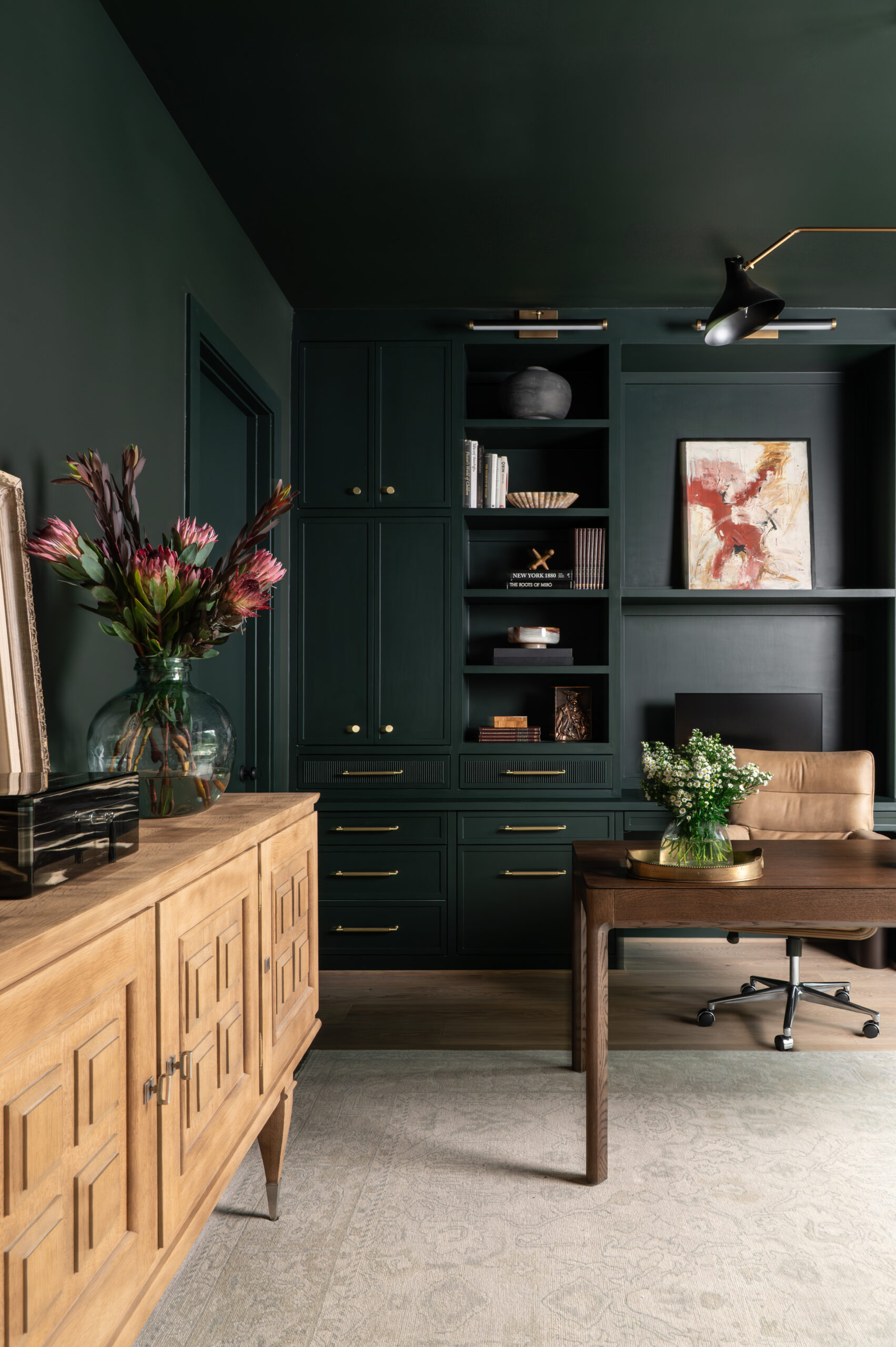 A dramatic home office with deep green built-ins, a leather desk chair, and wooden cabinetry, showing how lighting and layered finishes enhance the texture in interior design.
