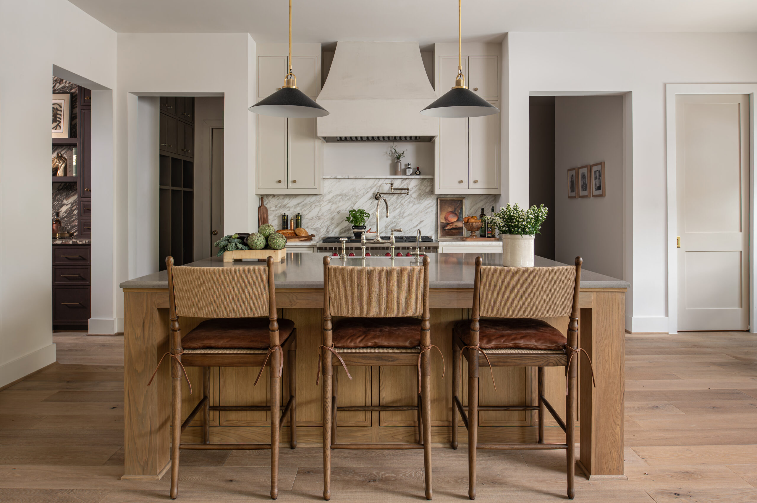 A modern kitchen with woven bar stools, leather seats, and natural wood tones, emphasizing texture in interior design by blending organic and refined materials throughout the space.