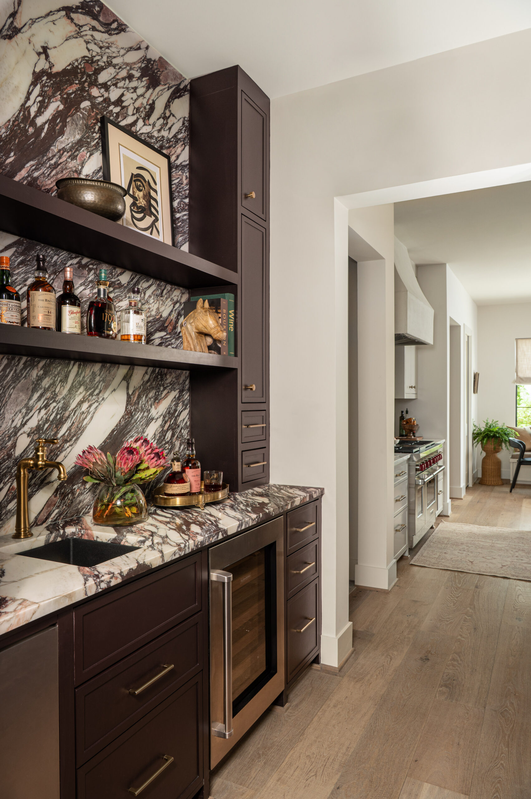 Marble backsplash and countertops add bold texture in interior design, paired with dark wood cabinetry, brass accents, and curated shelf styling.