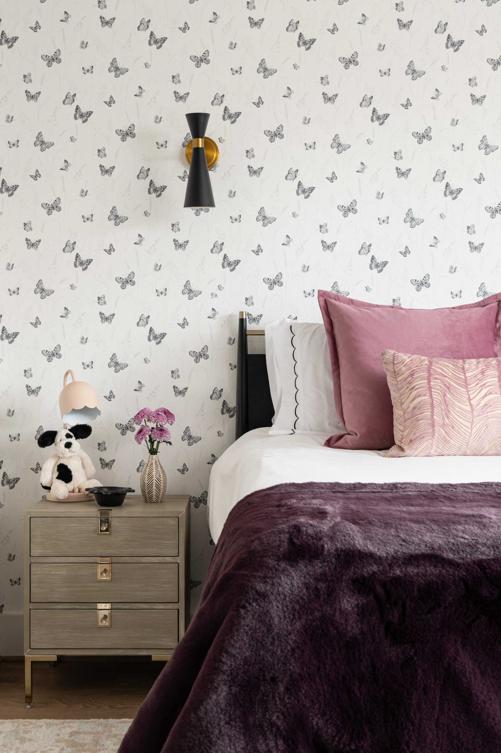 A whimsical kid’s bedroom with butterfly wallpaper, a velvet blanket, and contrasting cotton pillows that bring playful texture in interior design to life.