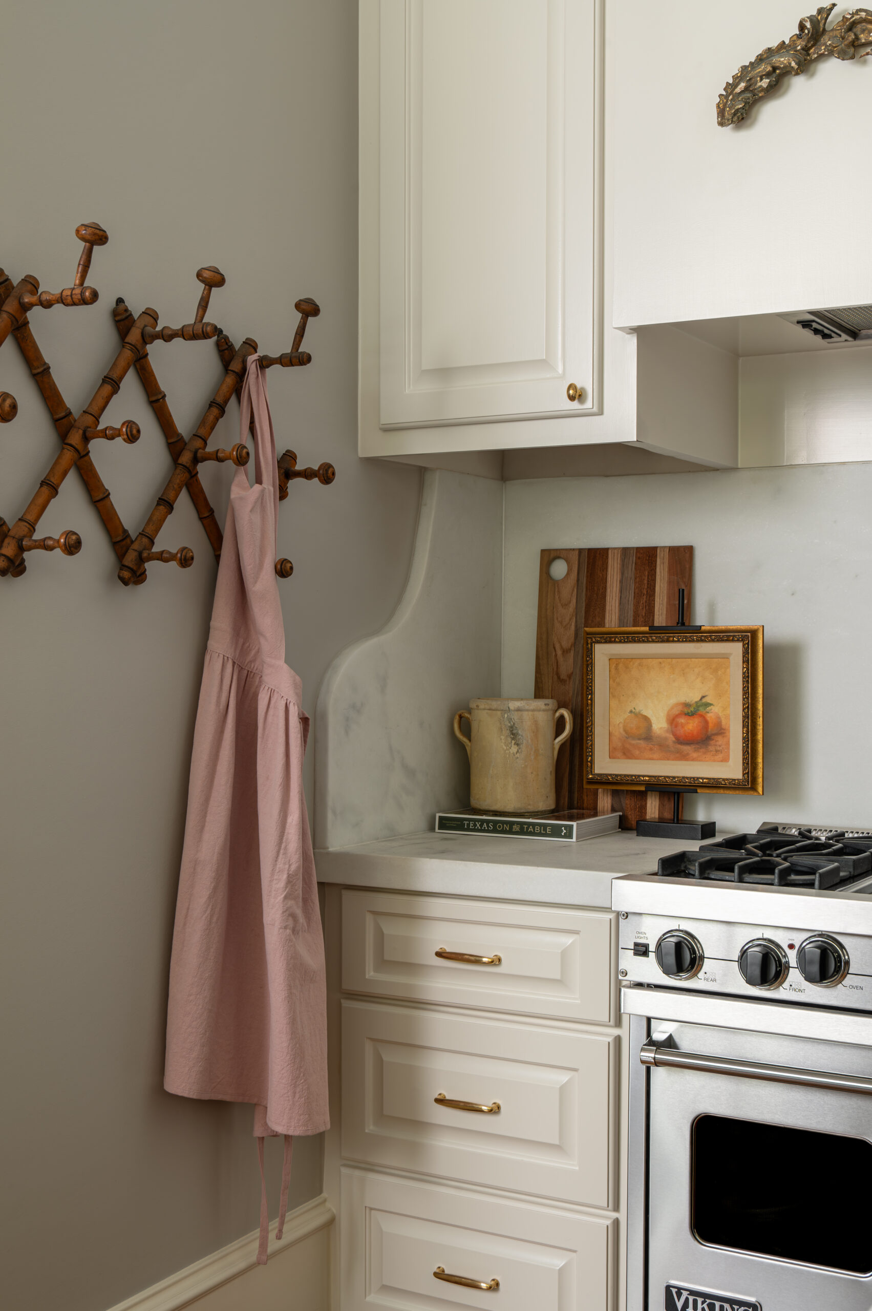 A close-up of the kitchen’s cozy corner featuring a blush pink apron, wooden cutting boards, vintage artwork, and subtle marble detailing—inviting warmth and functionality.