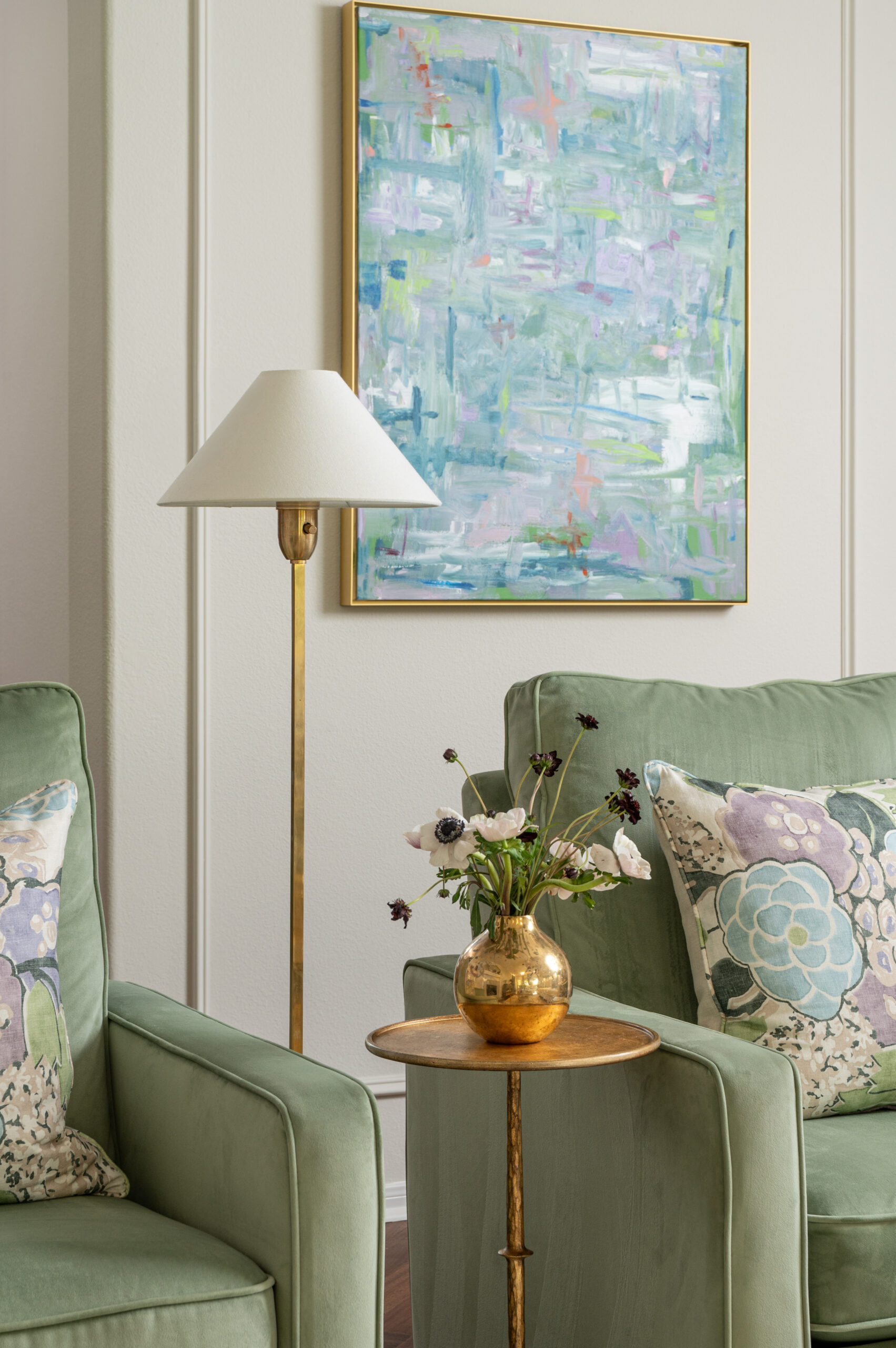 Artful interior shot featuring pastel abstract artwork, a vintage brass floor lamp, and modern floral styling on a side table for added depth.