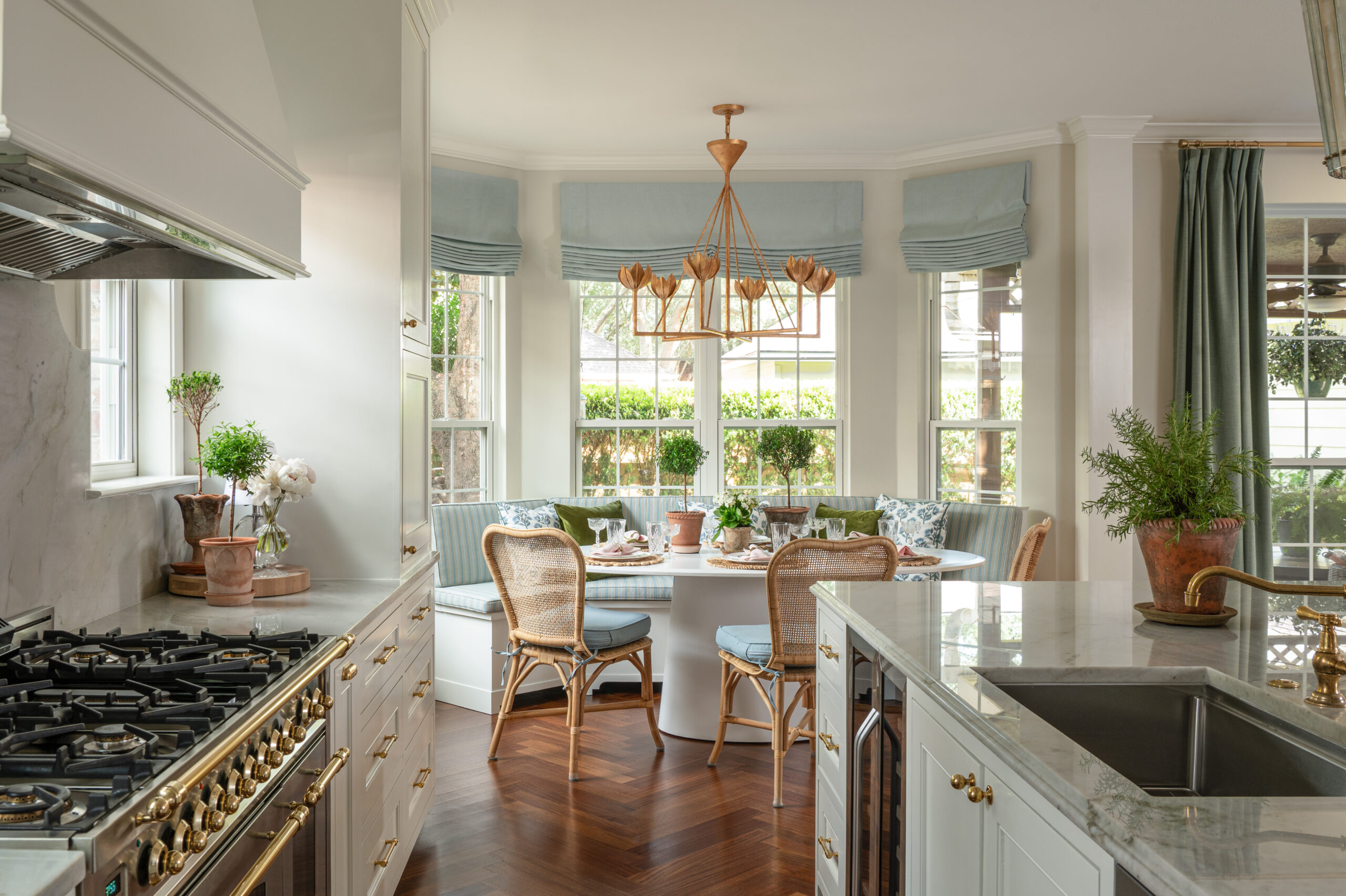 Bright kitchen view leading into a breakfast nook with built-in bench seating, blue roman shades, and natural wood accents.