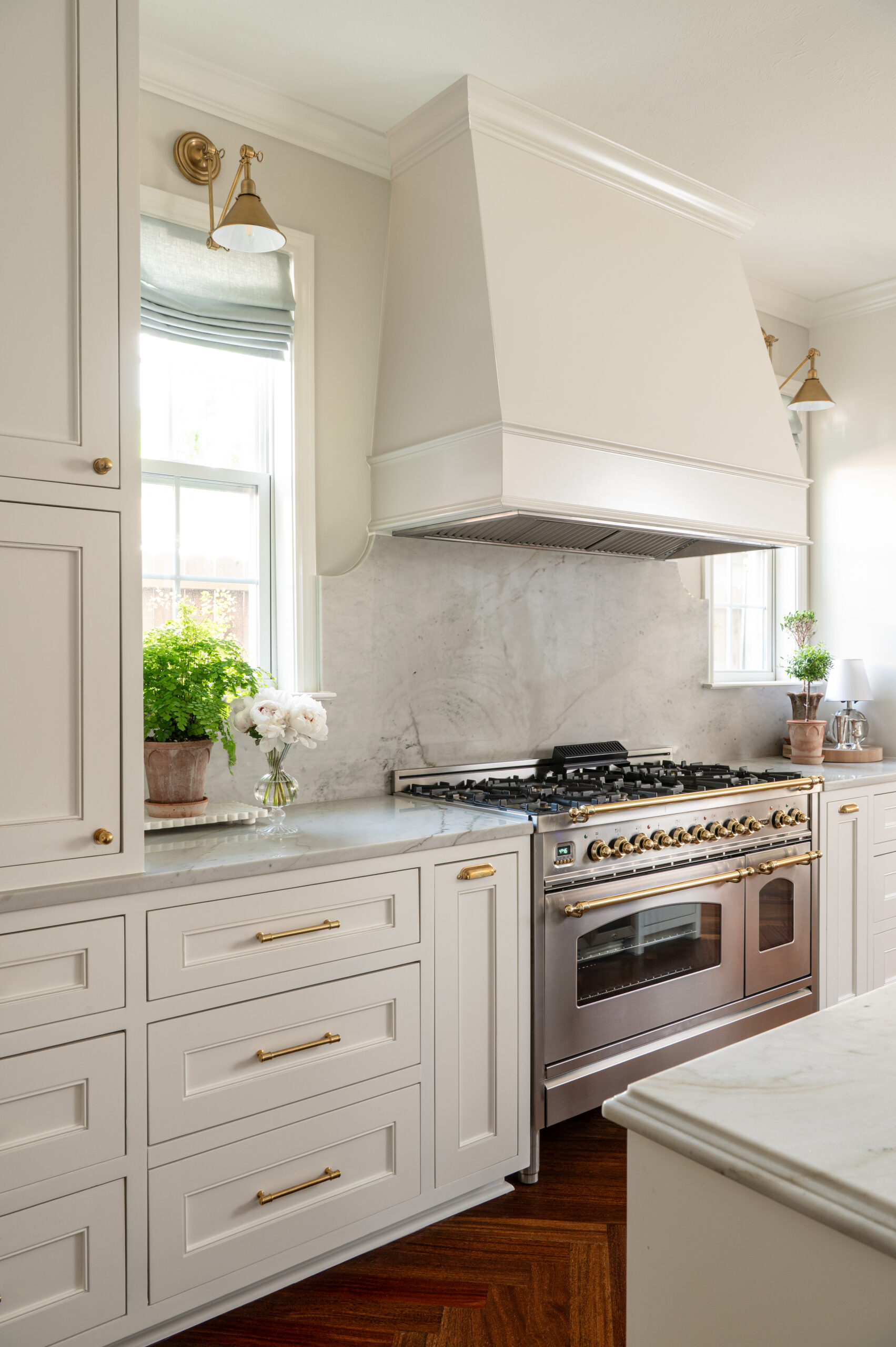 Elegant kitchen range framed by creamy cabinetry and soft gray marble, with unlacquered brass hardware adding a warm, collected feel.